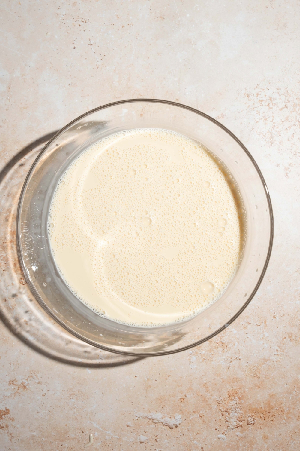 A large bowl with tres leches soak. The bowl is on a tan counter.