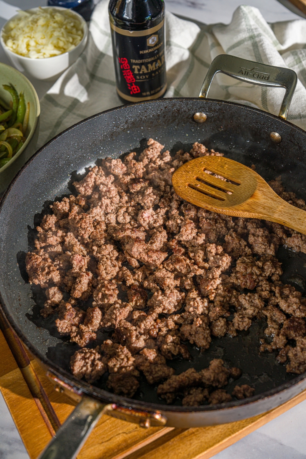 A skillet with a wooden spoon stirring browned ground beef. The skillet is on a wooden board.