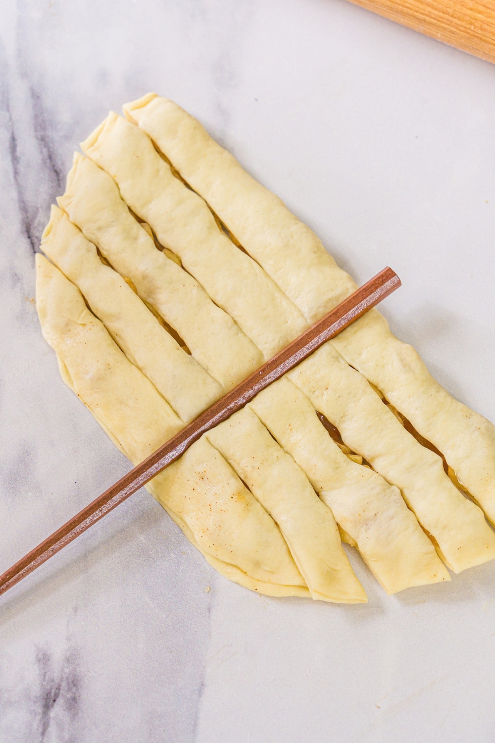A dough pocket filled with apple pie dough with a chopstick placed down the middle. The dough is sliced into horizontal strips.
