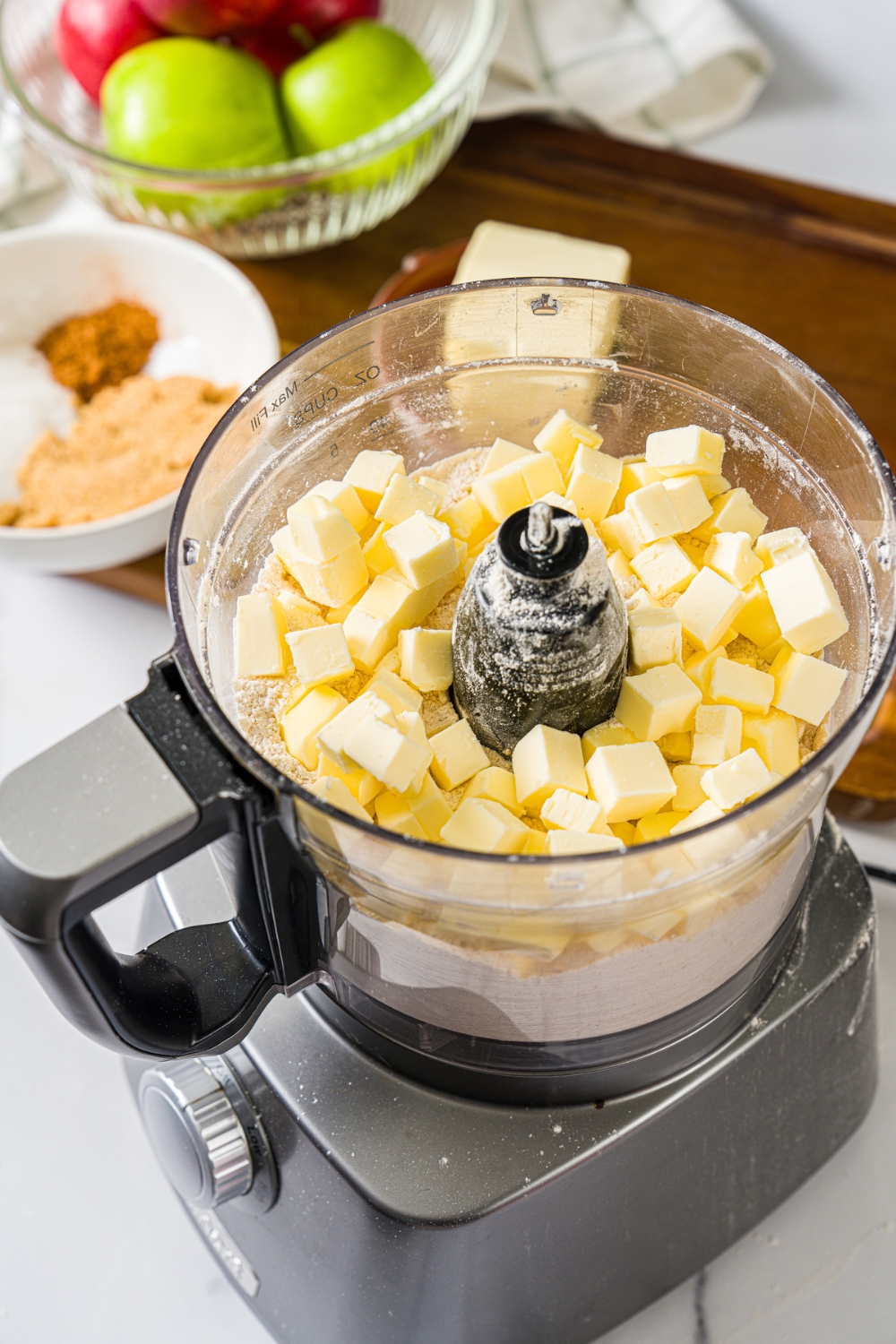 A food processor with cubed butter and dry ingredients to make cinnamon roll crust dough. The food processor is on a marble counter.