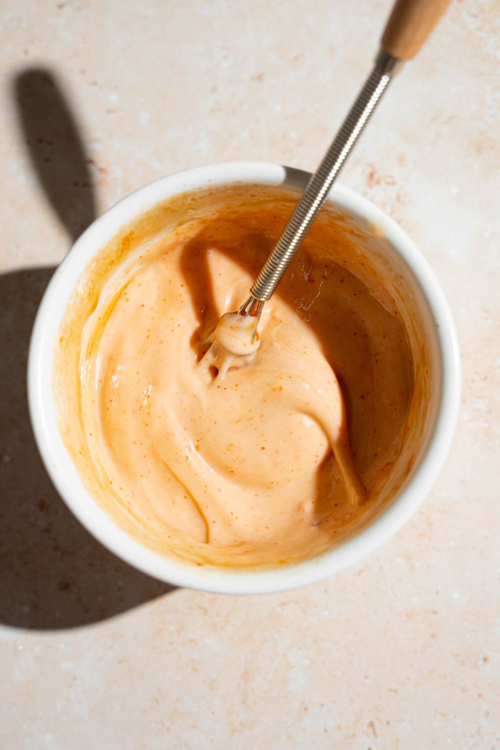 A large bowl with mixed bang bang sauce. There is a hand mixer in the sauce.