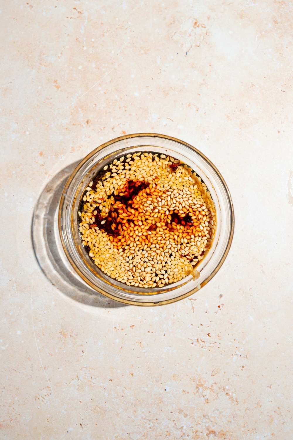 A small bowl with a sesame soil soy sauce dressing with sesame seeds. The bowl is on a tan counter.