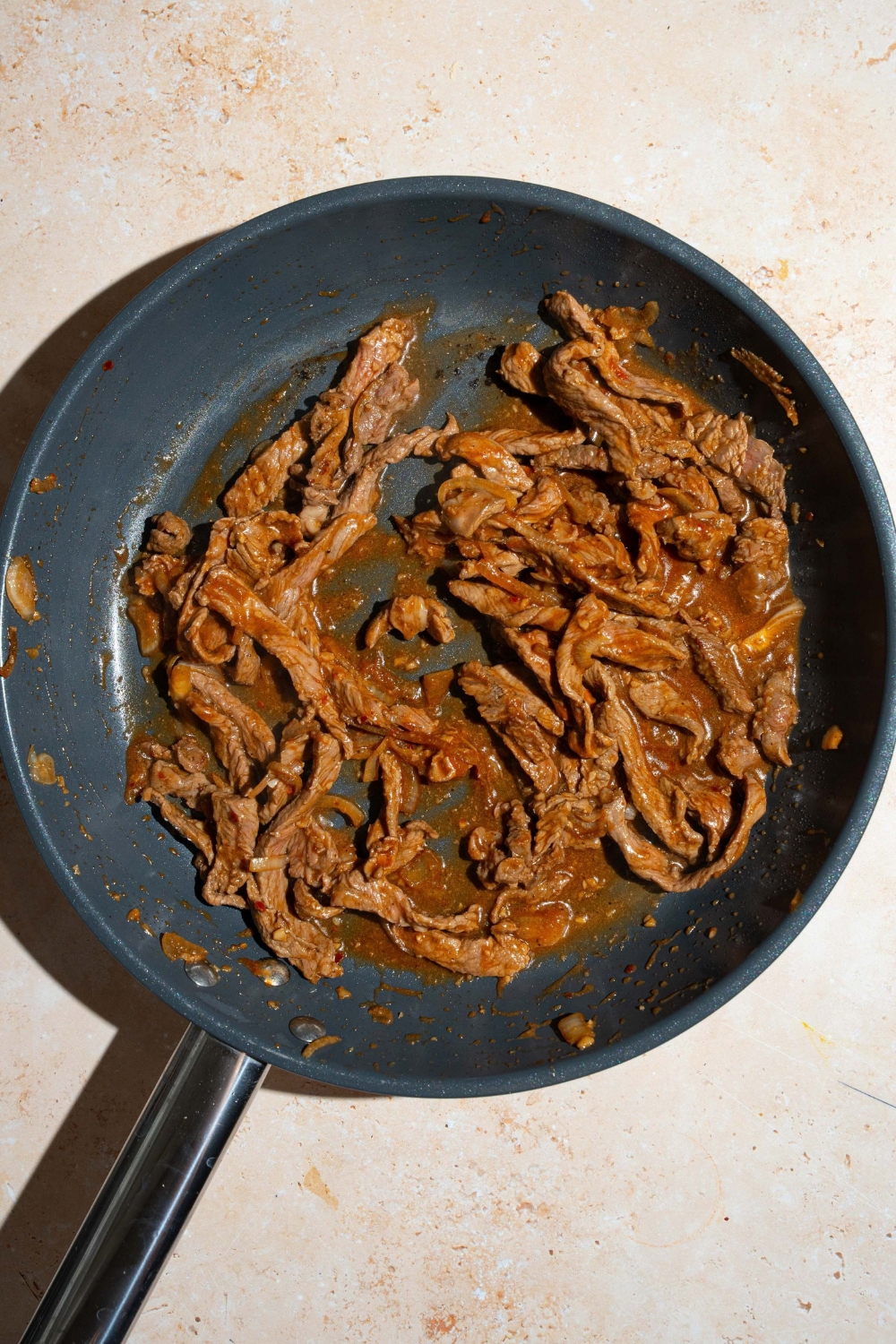 A skillet with cooked beef in bulgogi sauce. The skillet is on a tan counter.