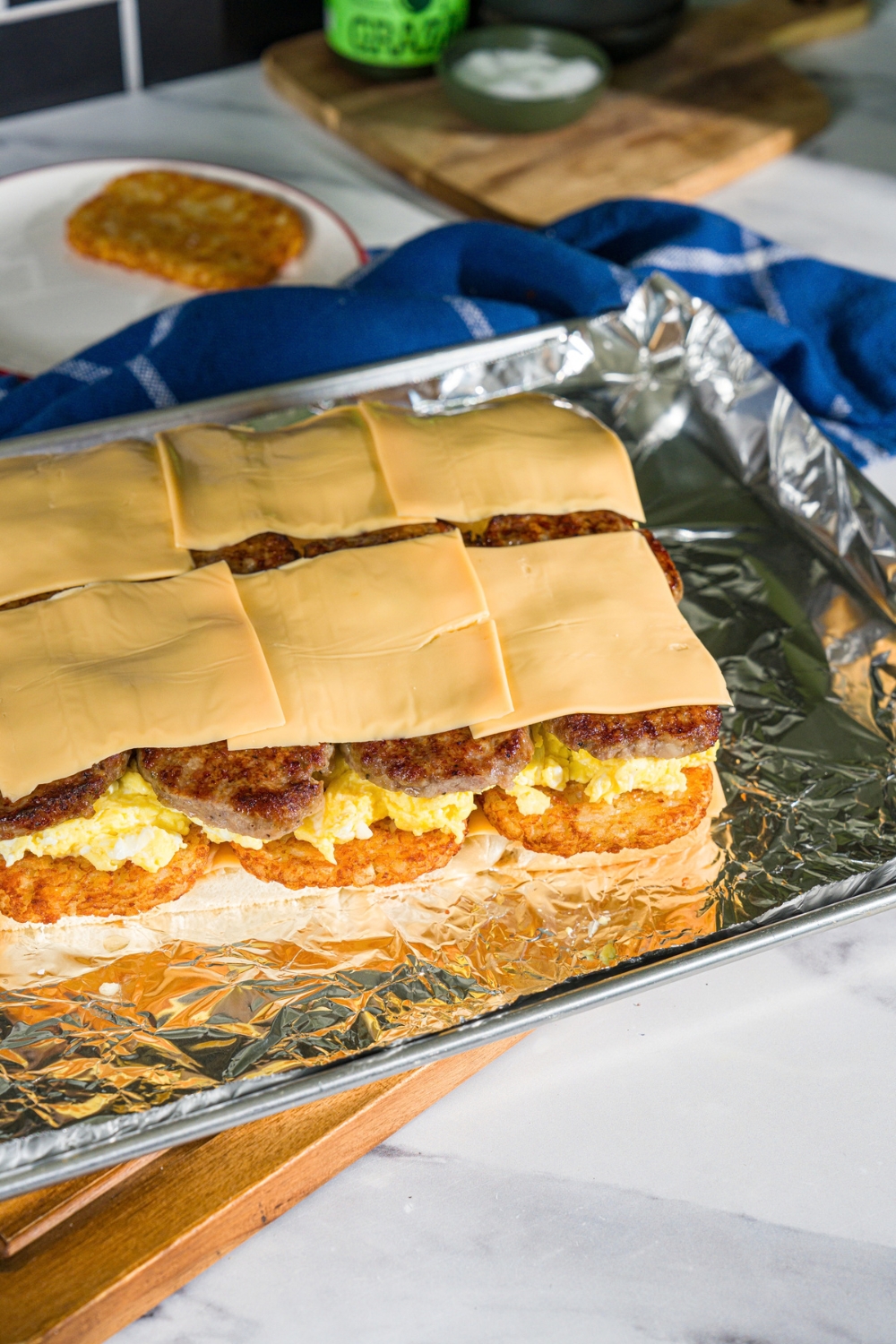 A baking sheet lined with foil with open breakfast sliders with hashbrowns, sausage, scrambled eggs, and cheese on hawaiian rolls.