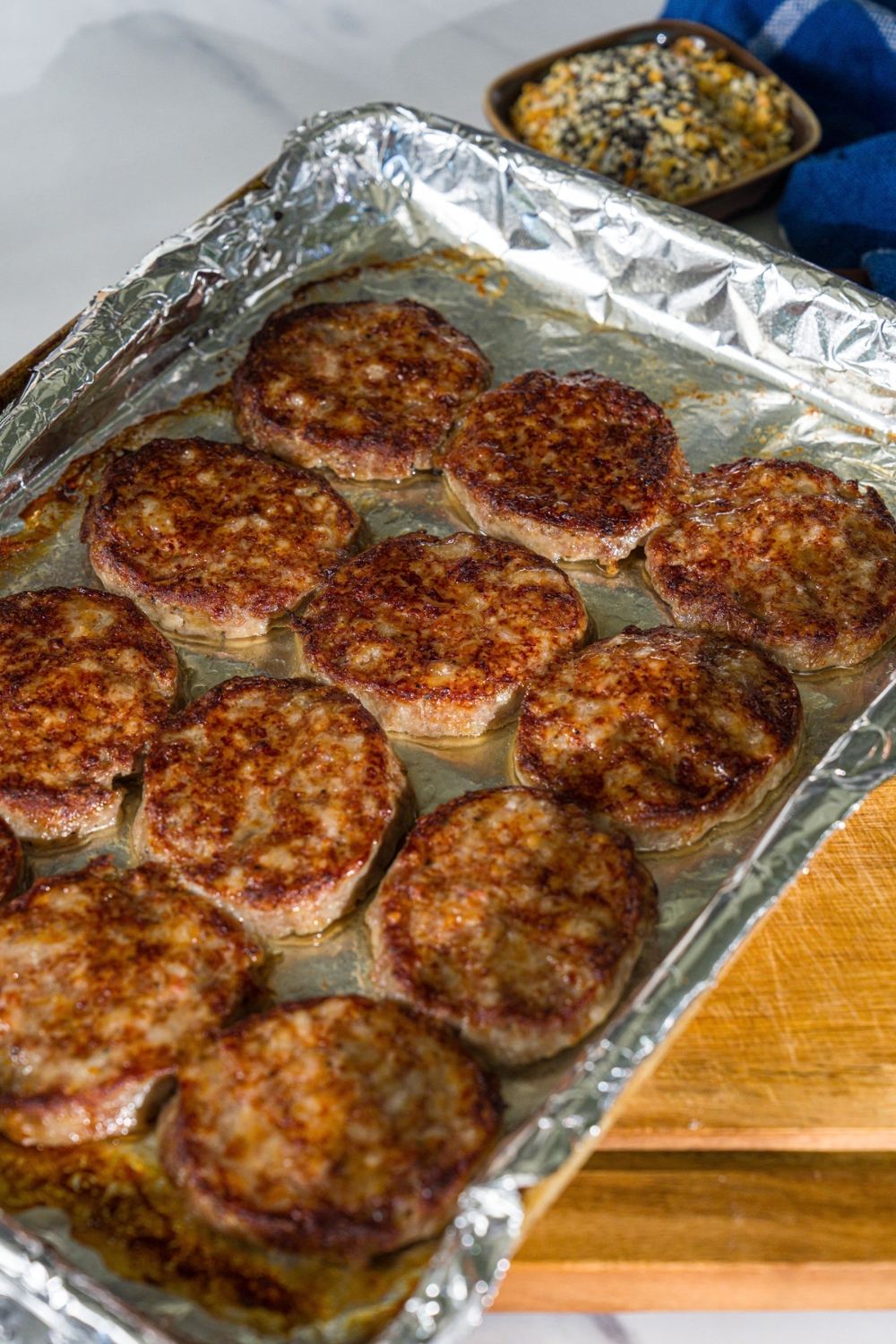 A baking sheet lined with foil with cooked breakfast sausage patties. The sheet is on a wooden board.