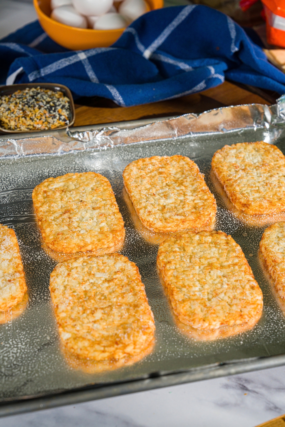 A baking sheet lined with foil with hashbrown patties. The sheet is on a marble counter.