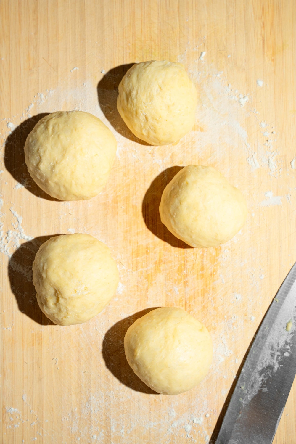 A wooden board with several dough balls for buns. The board is dusted with flour.