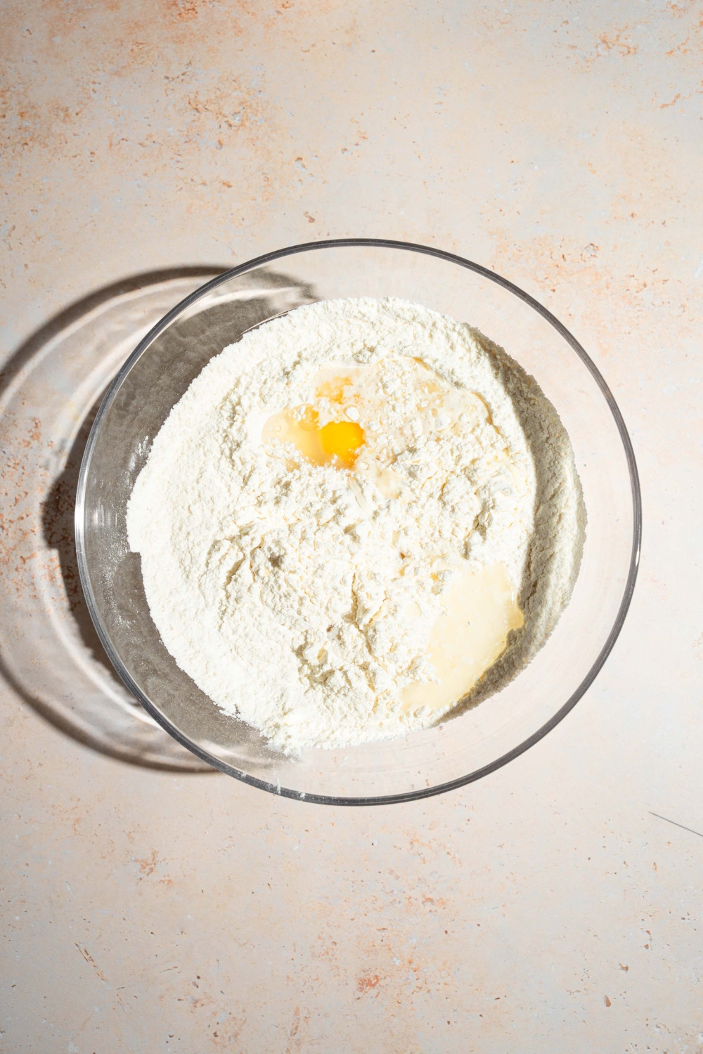 A large bowl with ingredients to make bun dough including flour, egg, water, yeast, and sugar. The bowl is on a tan counter.