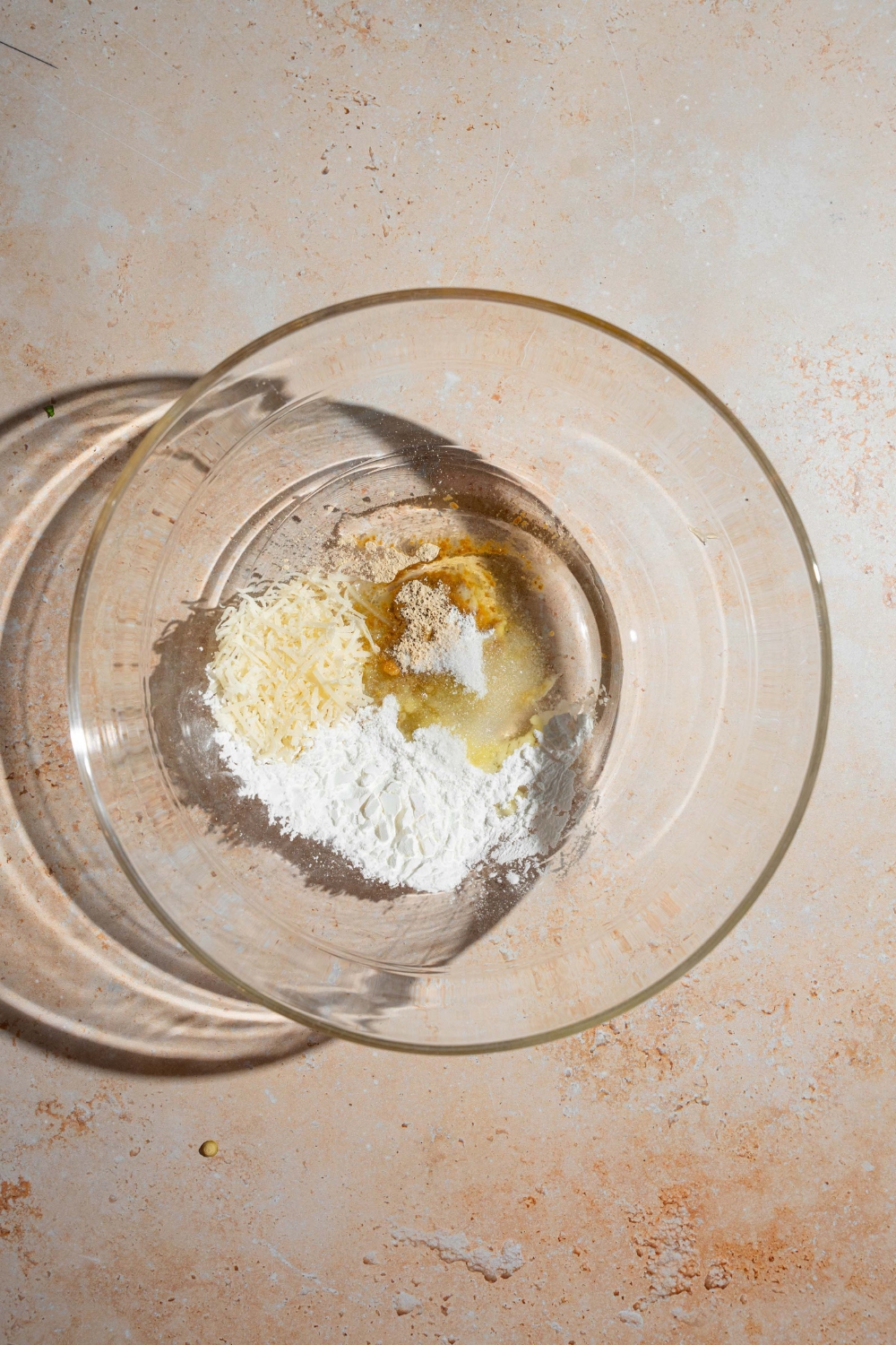 A large bowl with ingredients for carrot fry seasoning including oil, cornstarch, cheese, and seasonings. The bowl is on a tan counter.