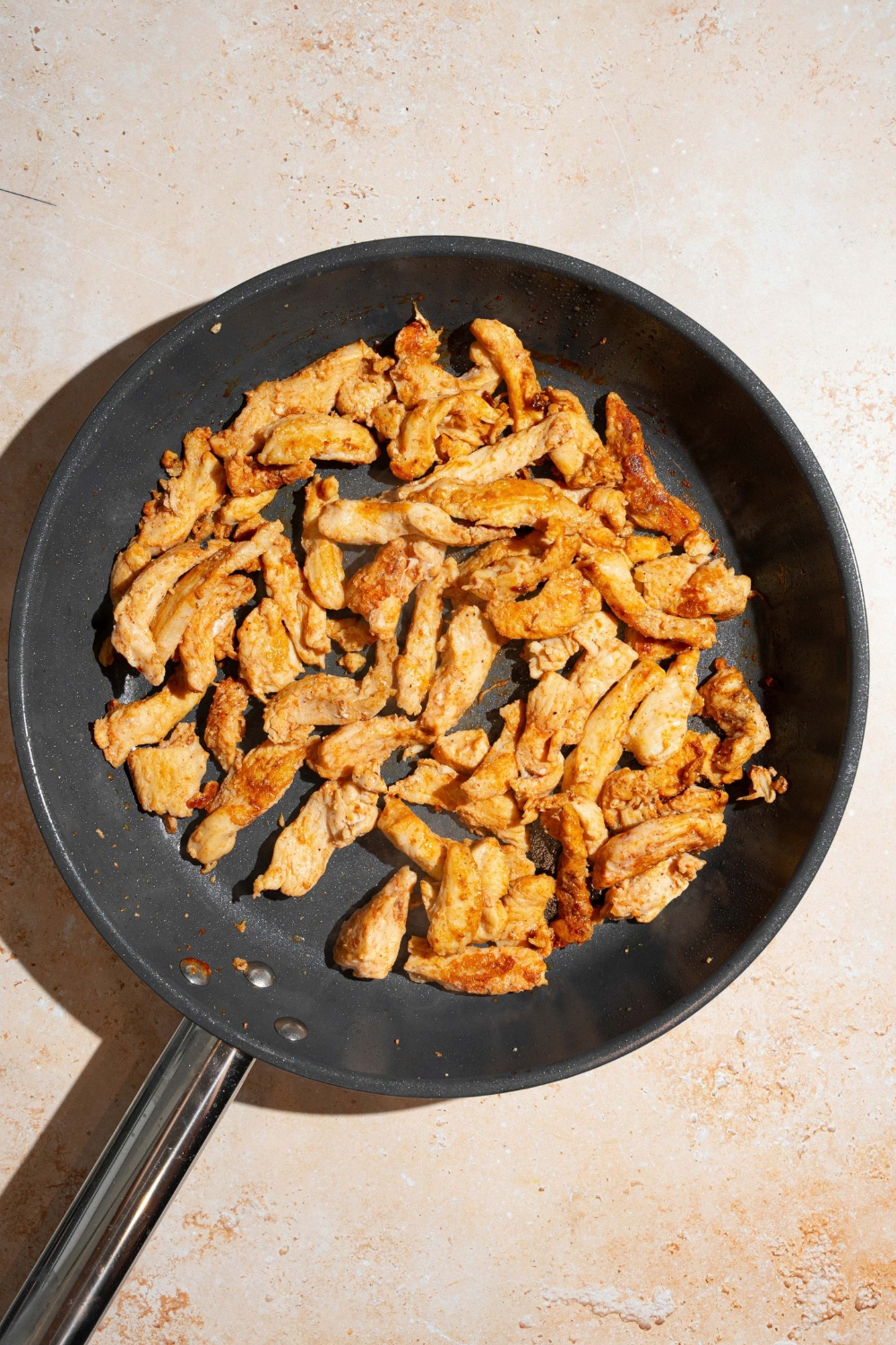 A skillet with seared seasoned chicken. The skillet is on a tan counter.