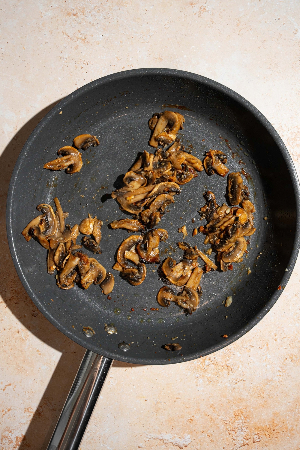A skillet with sautéed mushrooms with garlic and oil. The skillet is on a tan counter.