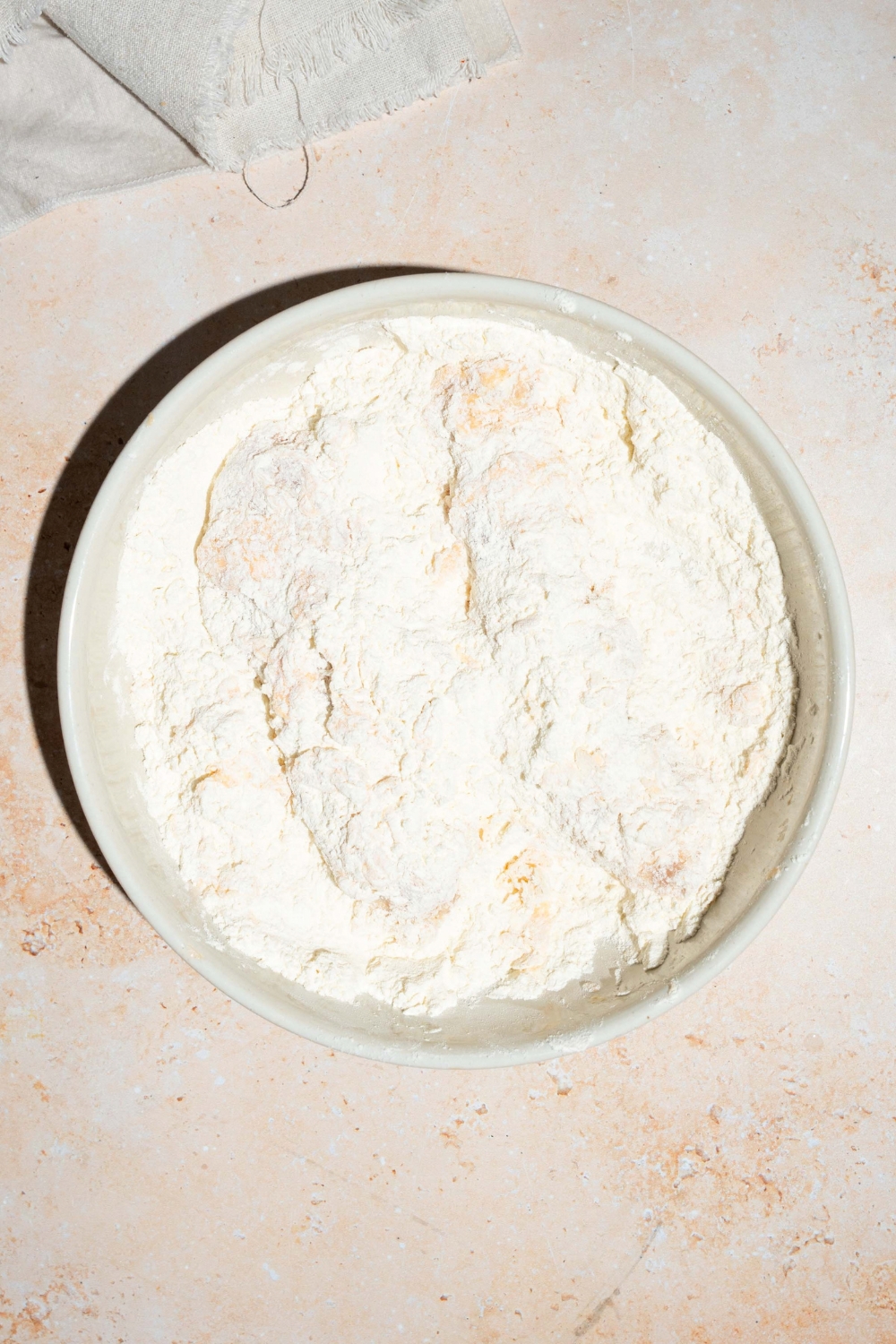 A white plate with marinated chicken tenders coated in flour. The plate is on a tan counter.