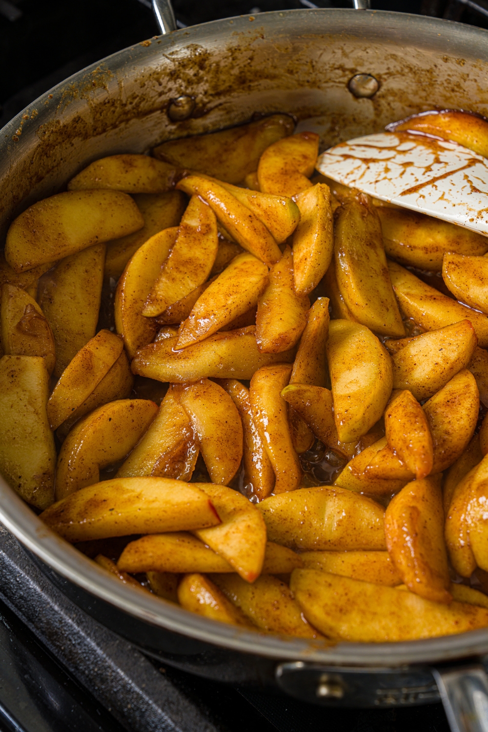A large pan with cooked apple pie filling including sliced apples with cinnamon and sugar. The skillet is cooking on the stove.