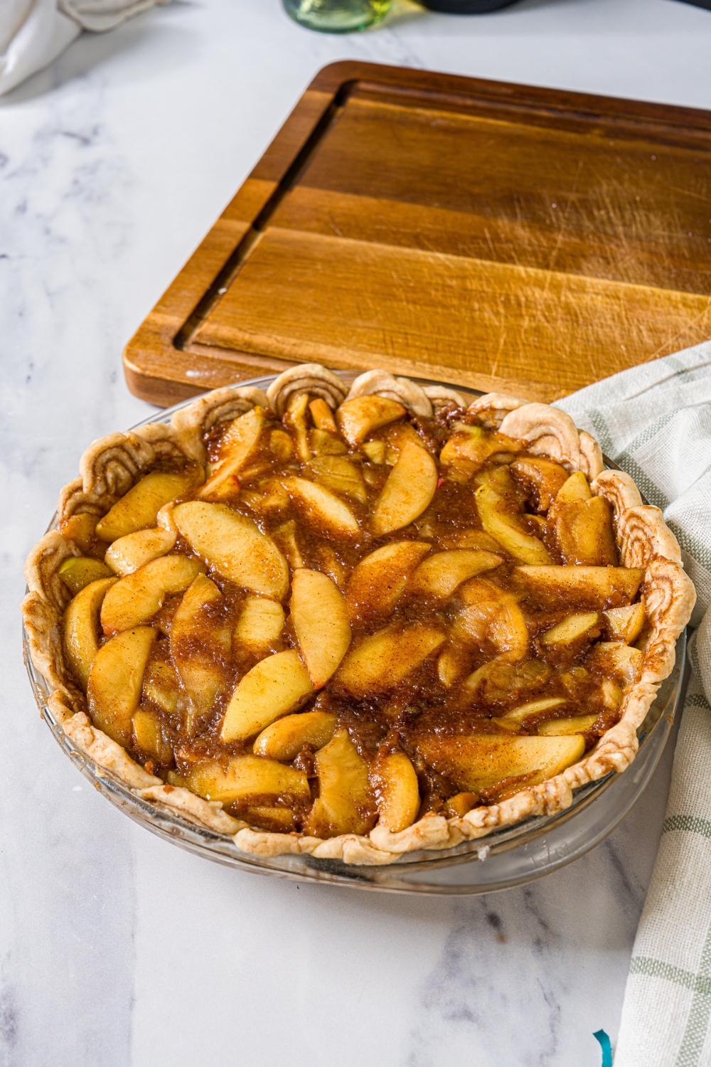 A pie dish with a cinnamon roll bottom crust and apple pie filling on top. The dish is on a marble counter with a wooden board.