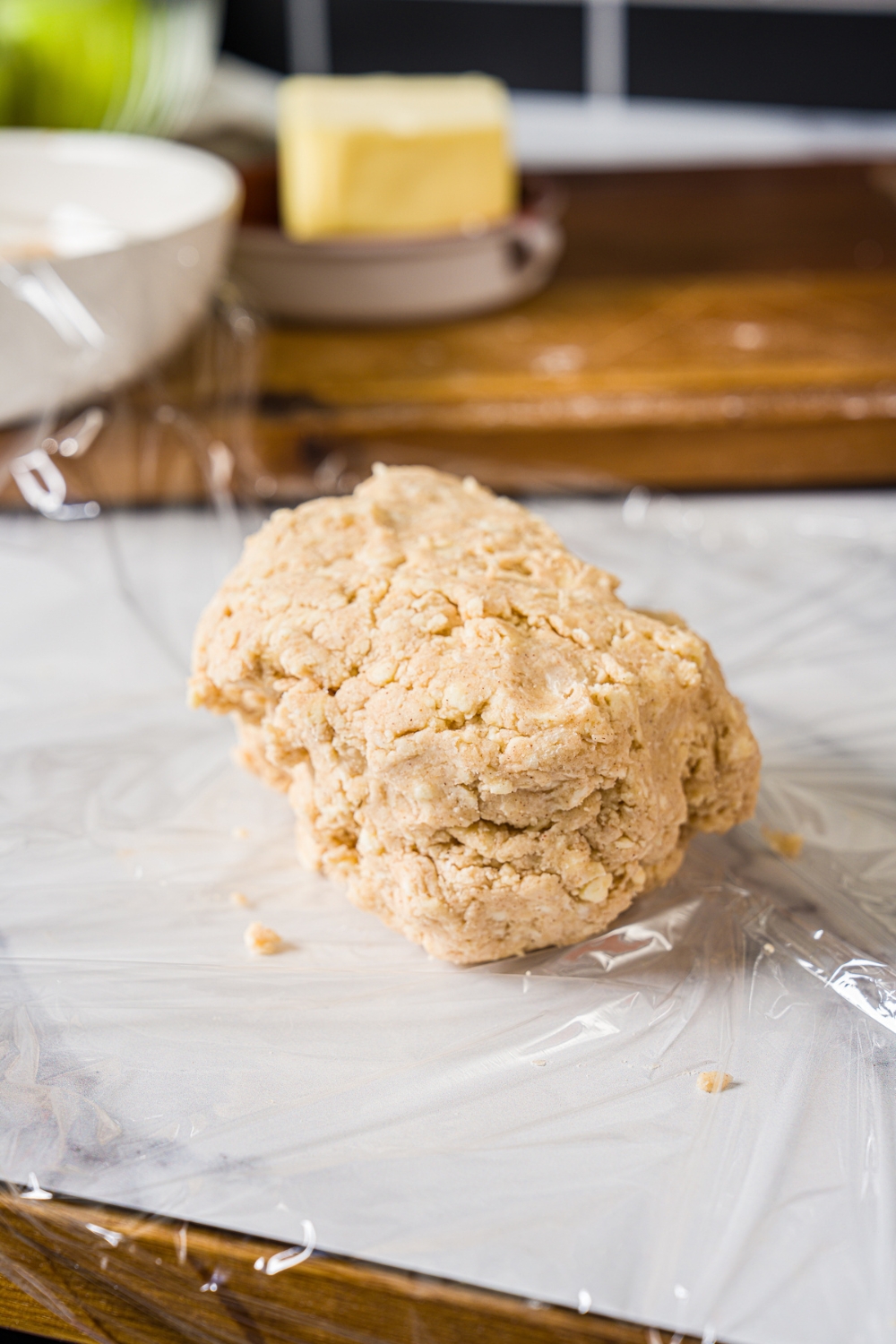 A cinnamon roll crust dough ball on a piece of saran wrap on a marble counter.