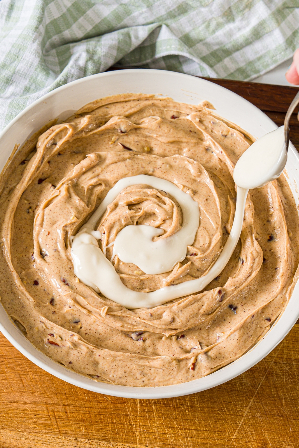 Icing being drizzled on top of cinnamon roll dip that's in a white bowl.