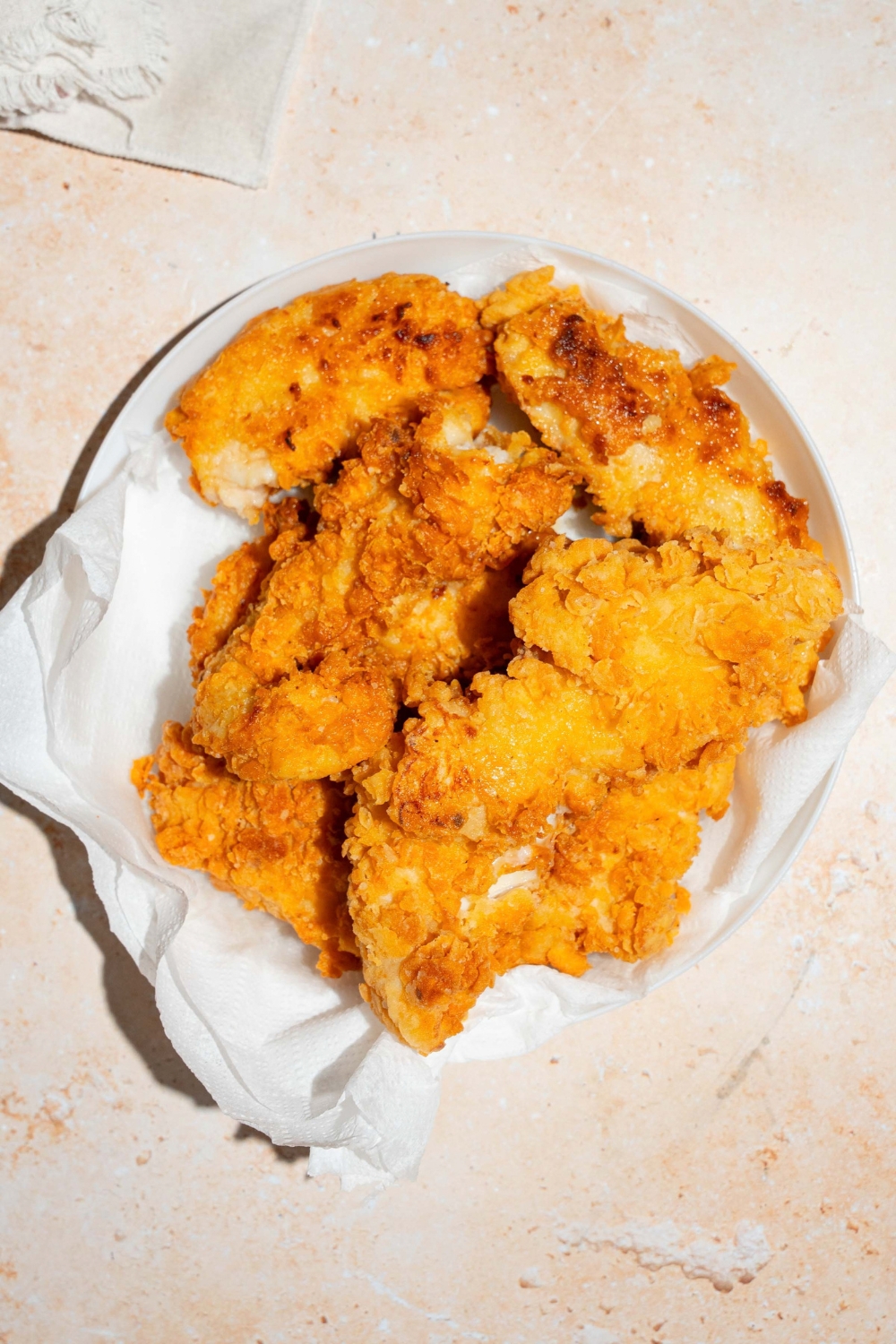 A white plate lined with paper towels with fried copycat Chick-Fil-A tenders. The plate is on a tan counter.