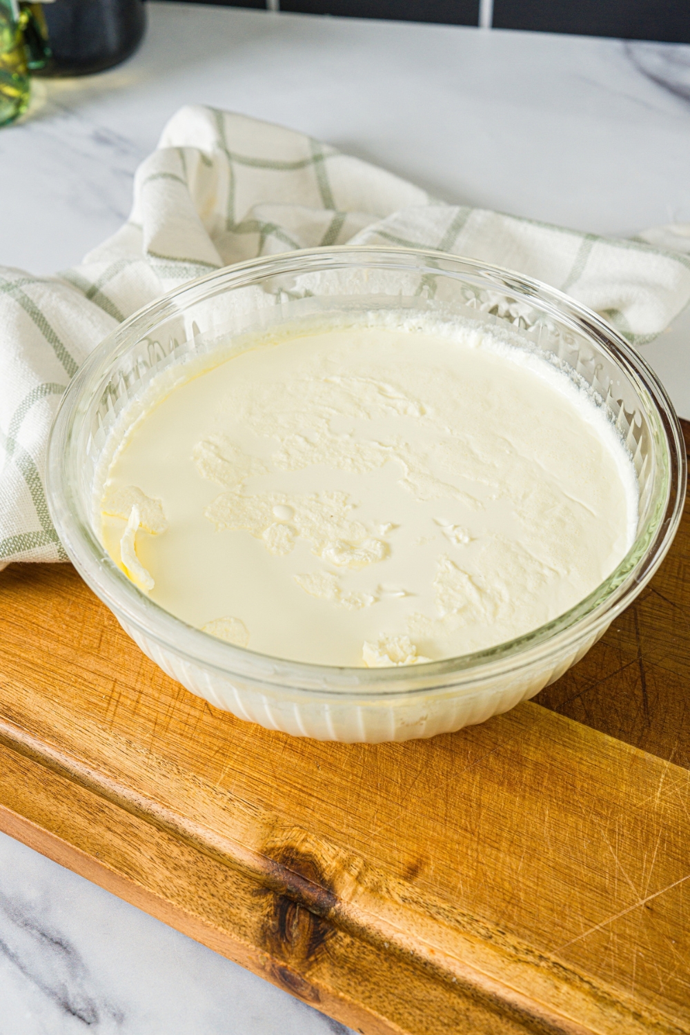 A large bowl with a cream and yogurt mixture. The bowl is on a wooden board with a white cloth napkin.