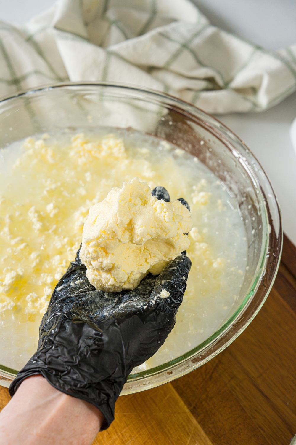 A large glass bowl with cultured butter mixture submerged in an ice bath. A hand is removing some of the solidified butter from the bowl.