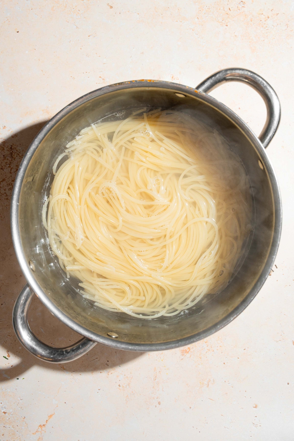 A large pot with spaghetti cooking in water. The pot is on a tan counter.
