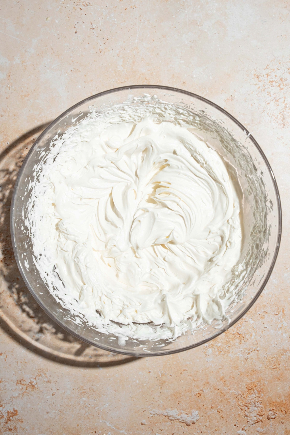A large bowl with whipped cream. The bowl is on a tan counter.