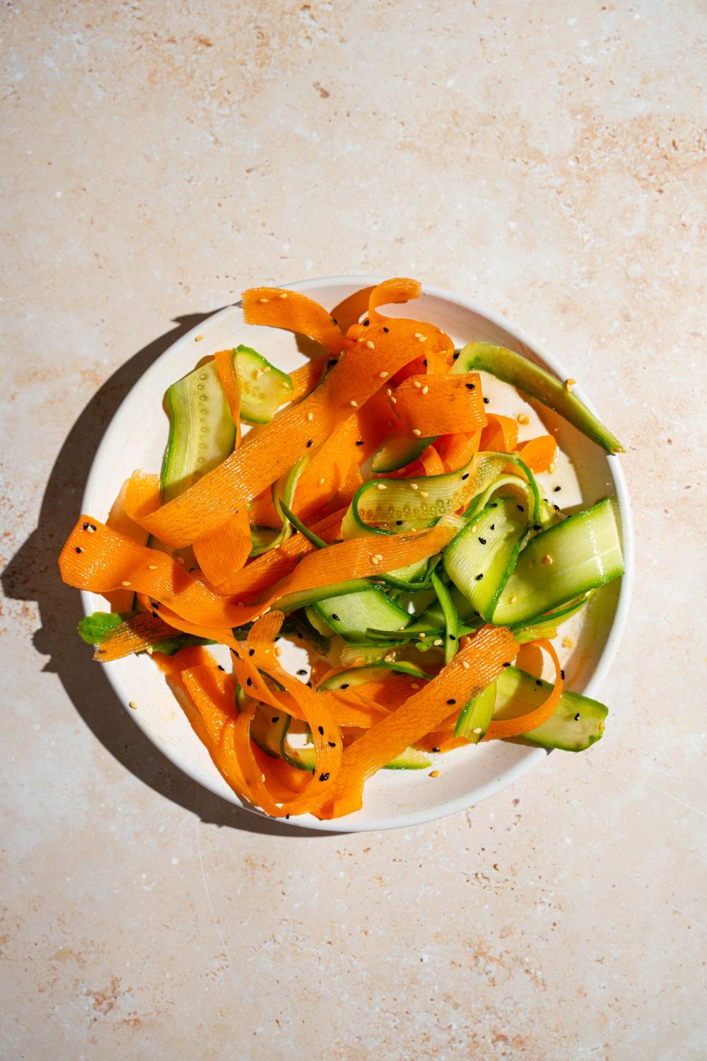 A white plate with carrot and cucumber ribbons tossed in a honey and rice vinegar dressing. The plate is on a tan counter.