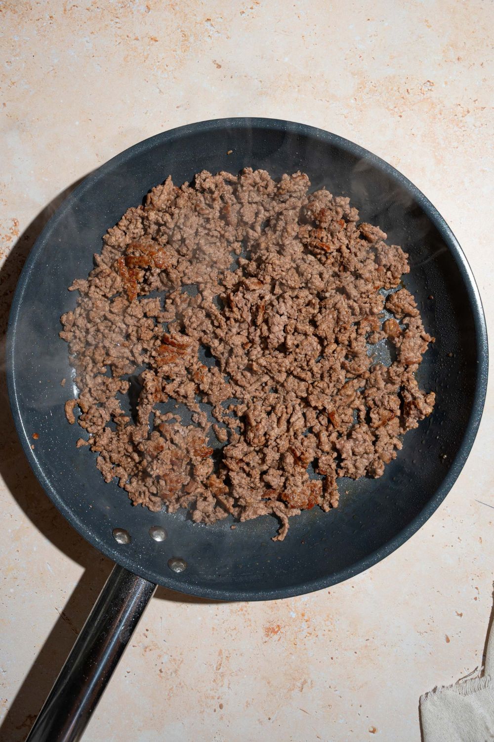 A skillet with cooked ground beef. The skillet is on a tan counter.