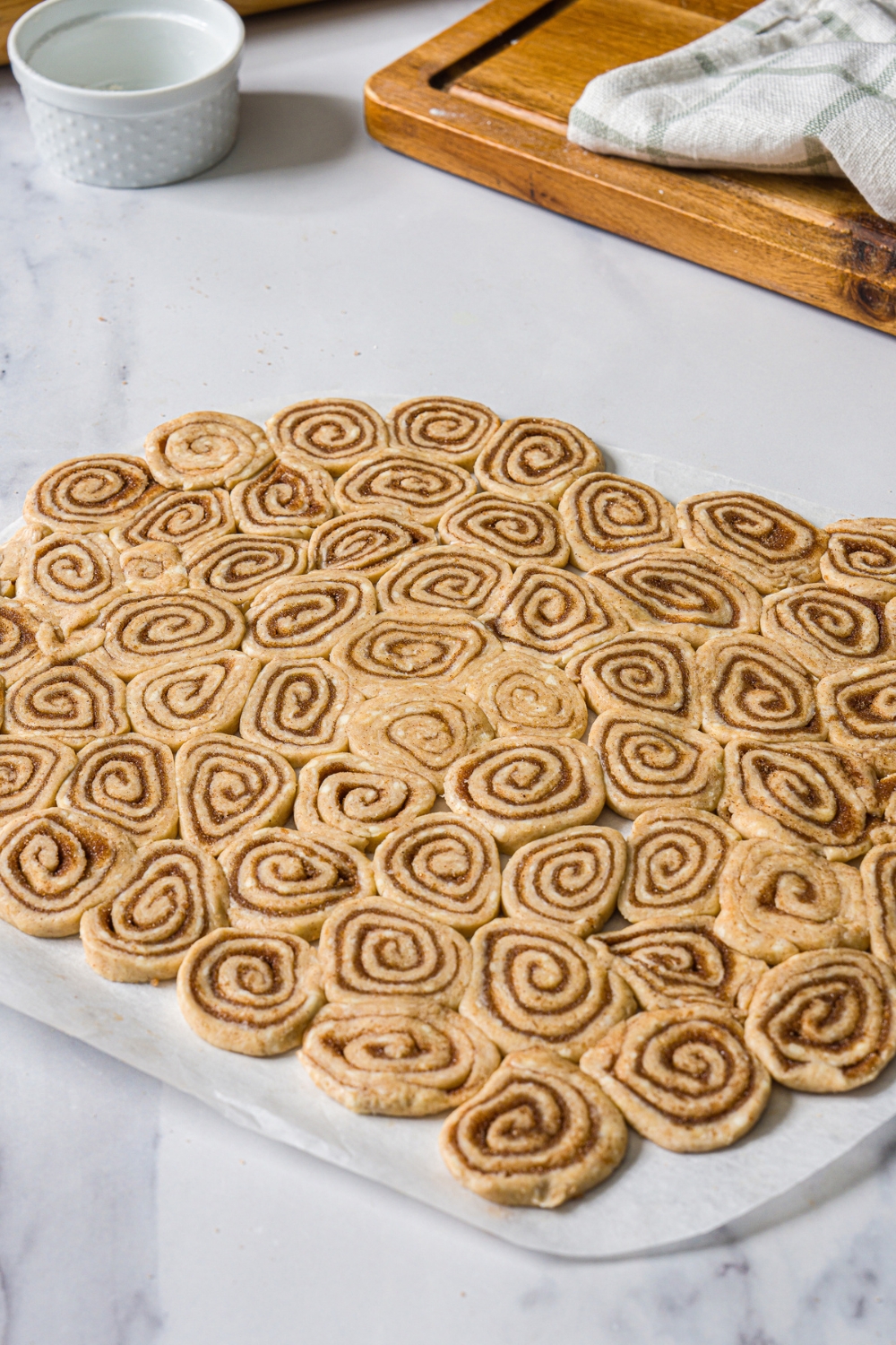 A piece of parchment paper with slices of cinnamon roll pieces shaped into a top crust. The paper is on a marble counter.