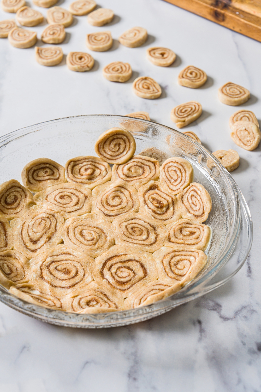 A greased glass pie dish with slices of cinnamon roll dough covering the plate. The plate is on a marble counter.