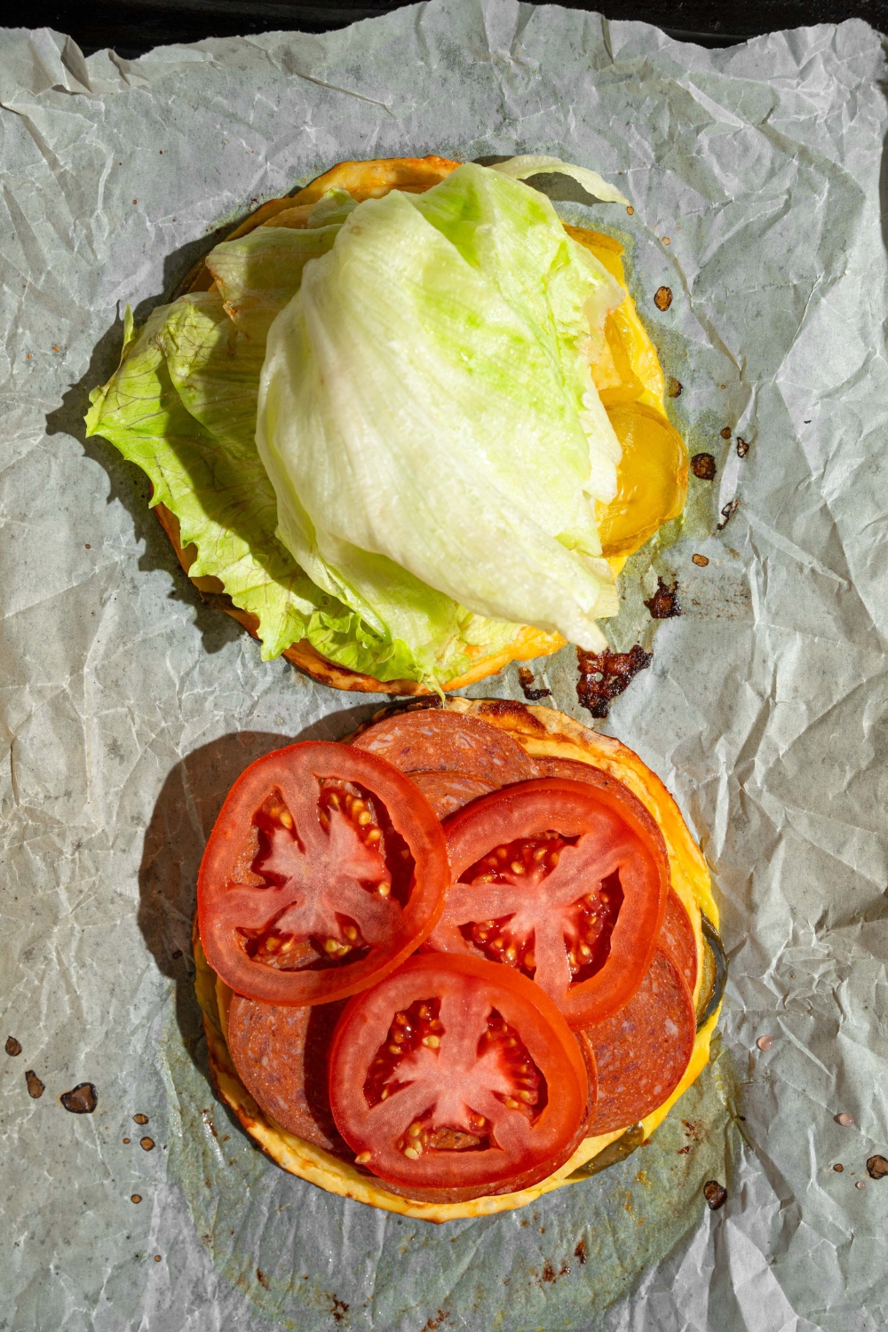 A baking sheet lined with parchment paper with two slices of pickle bread topped with lettuce, tomato, and deli meat.
