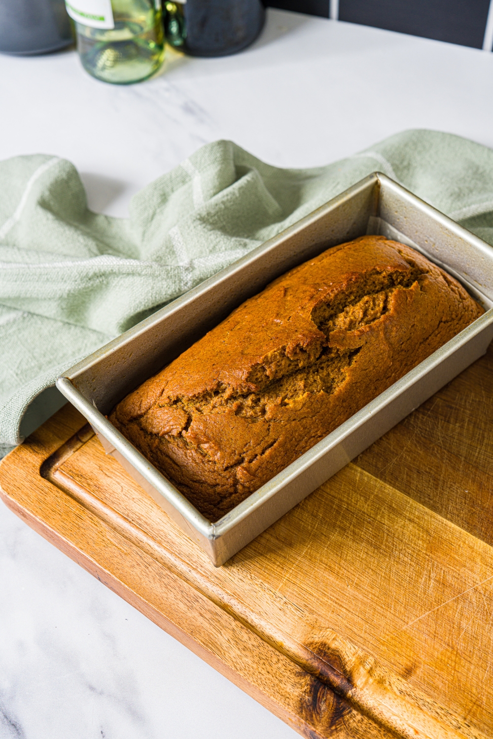 A loaf pan with baked pumpkin bread. The pan is on a wooden board with a green cloth napkin.