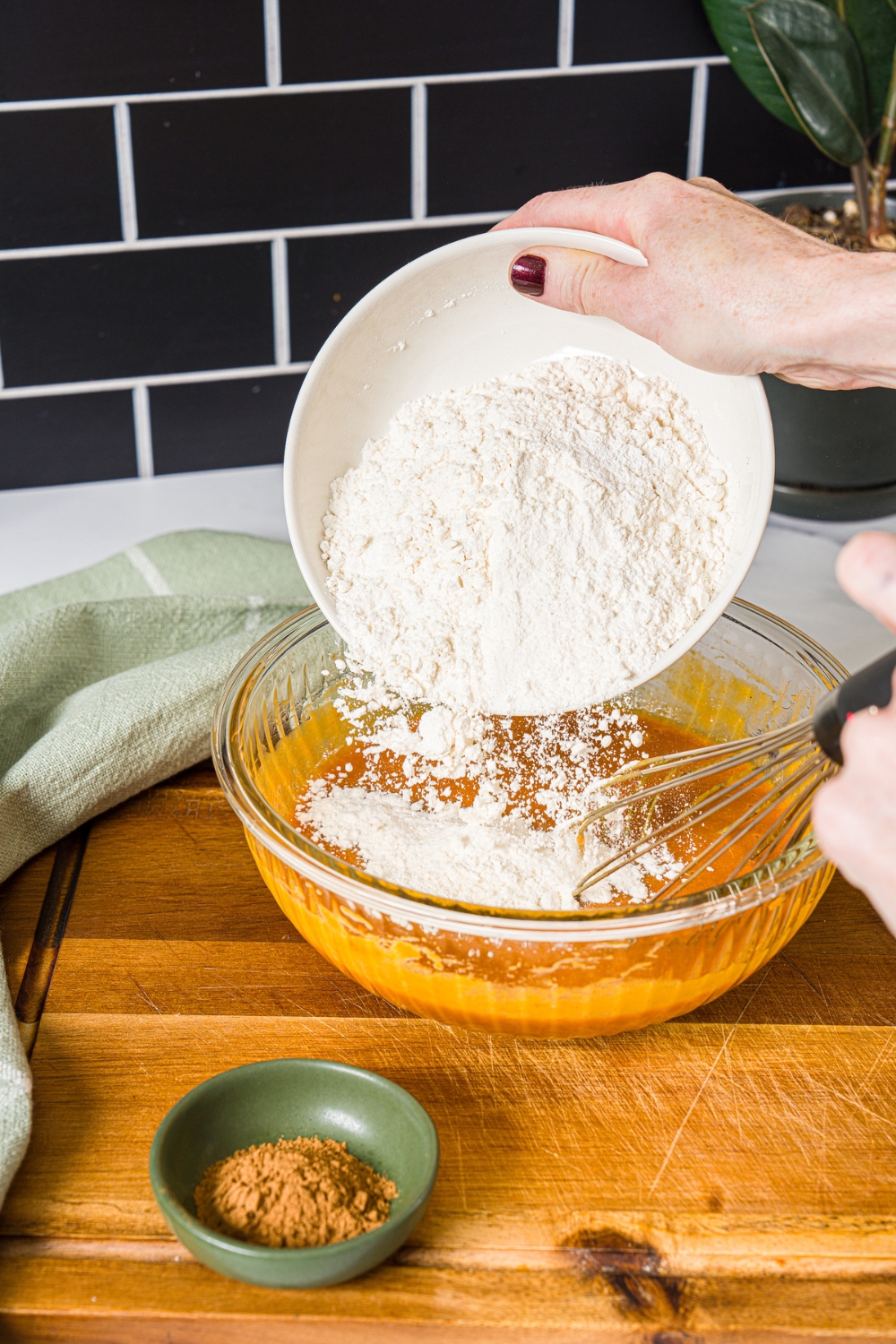 A large bowl with dry ingredients being added to a pumpkin batter mixture. The bowl is on a wooden board.