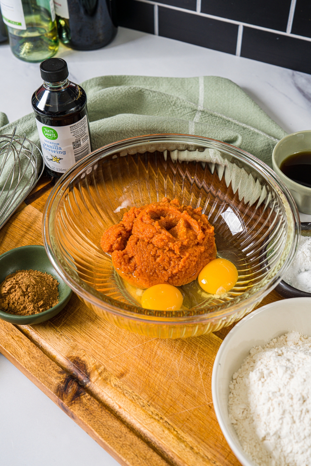 A large bowl with pumpkin puree and eggs. The bowl is on a wooden board with ingredients.