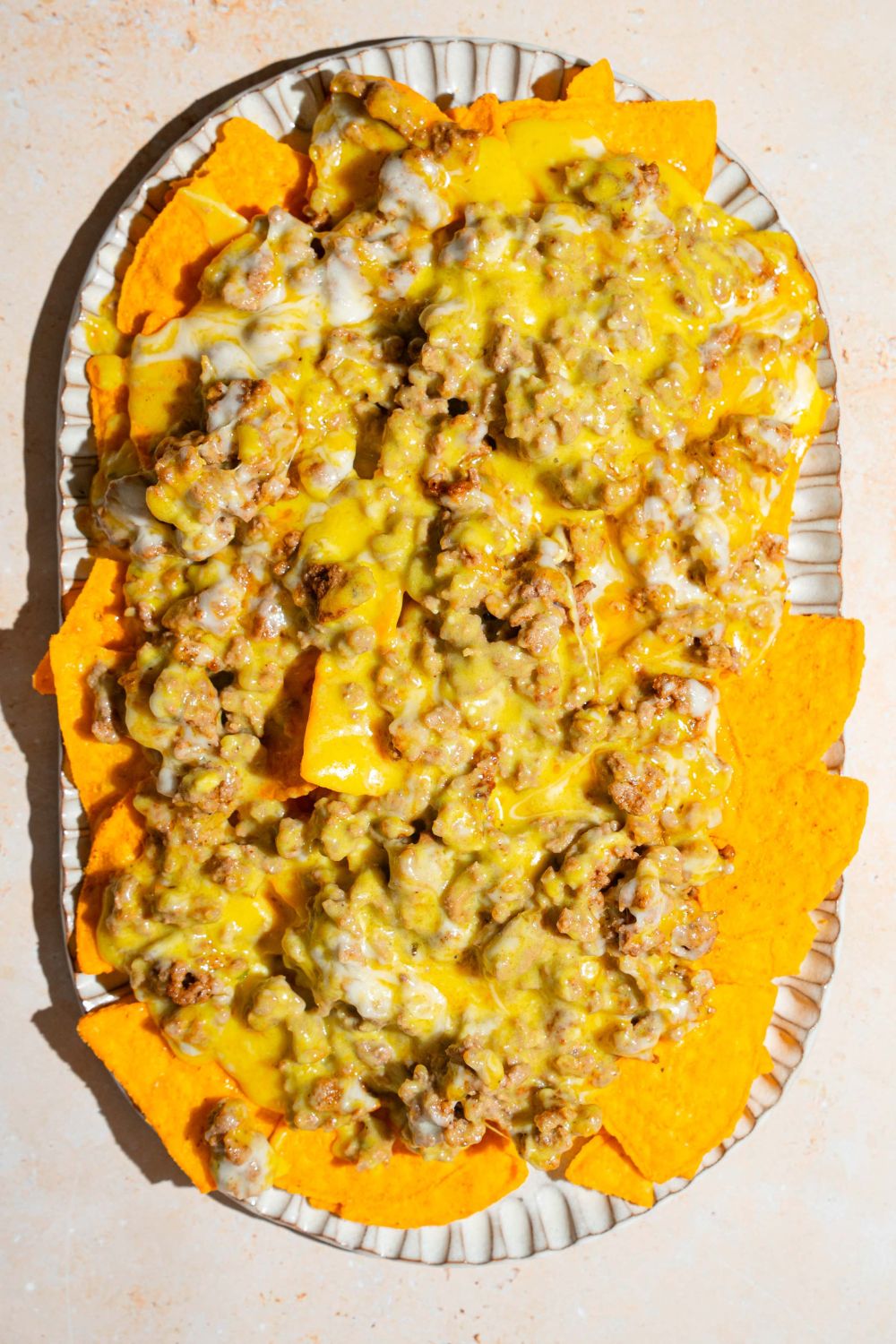 An oval platter with tortilla chips topped with sliding cheese with ground beef. The platter is on a tan counter.