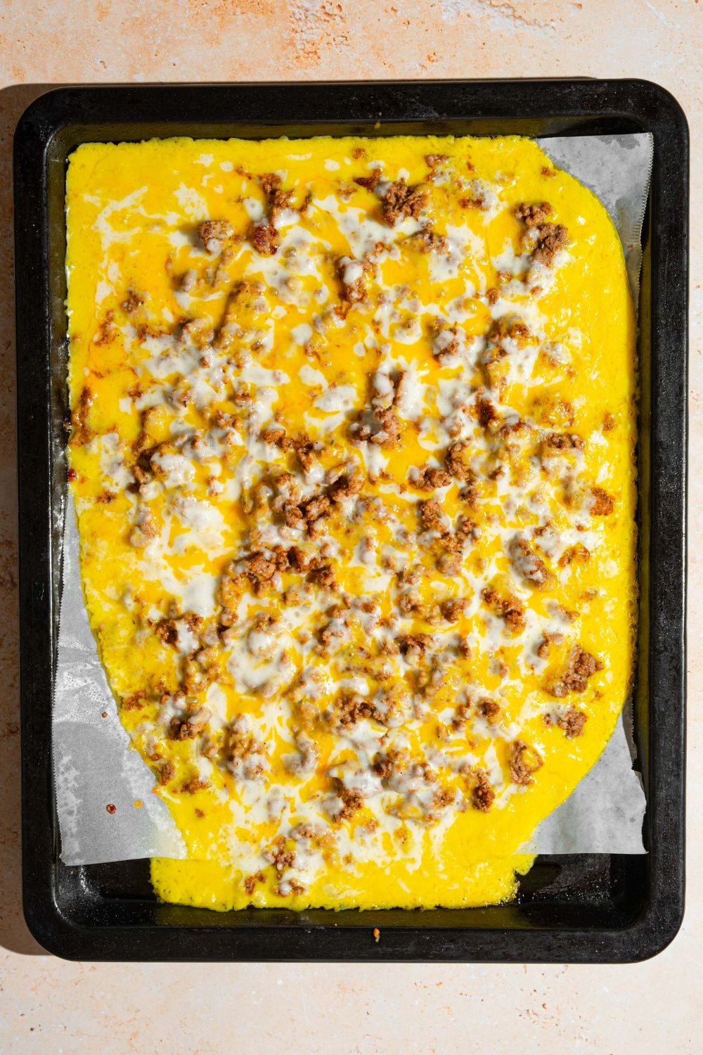 A baking tray lined with parchment paper with baked nacho cheese topped with ground beef and melted cheese. The tray is on a tan counter.