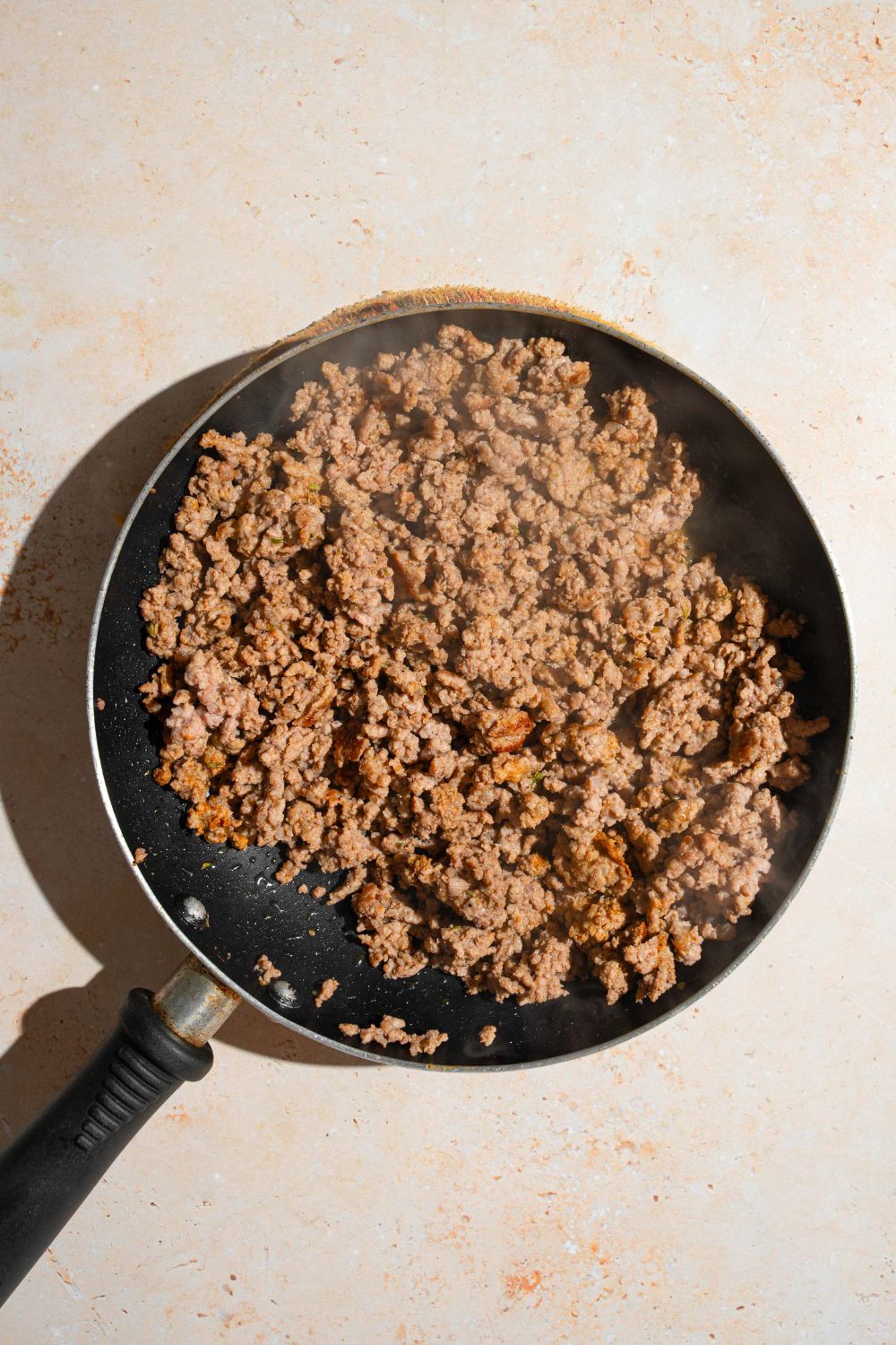 A skillet with seasoned ground beef. The skillet is on a tan counter.