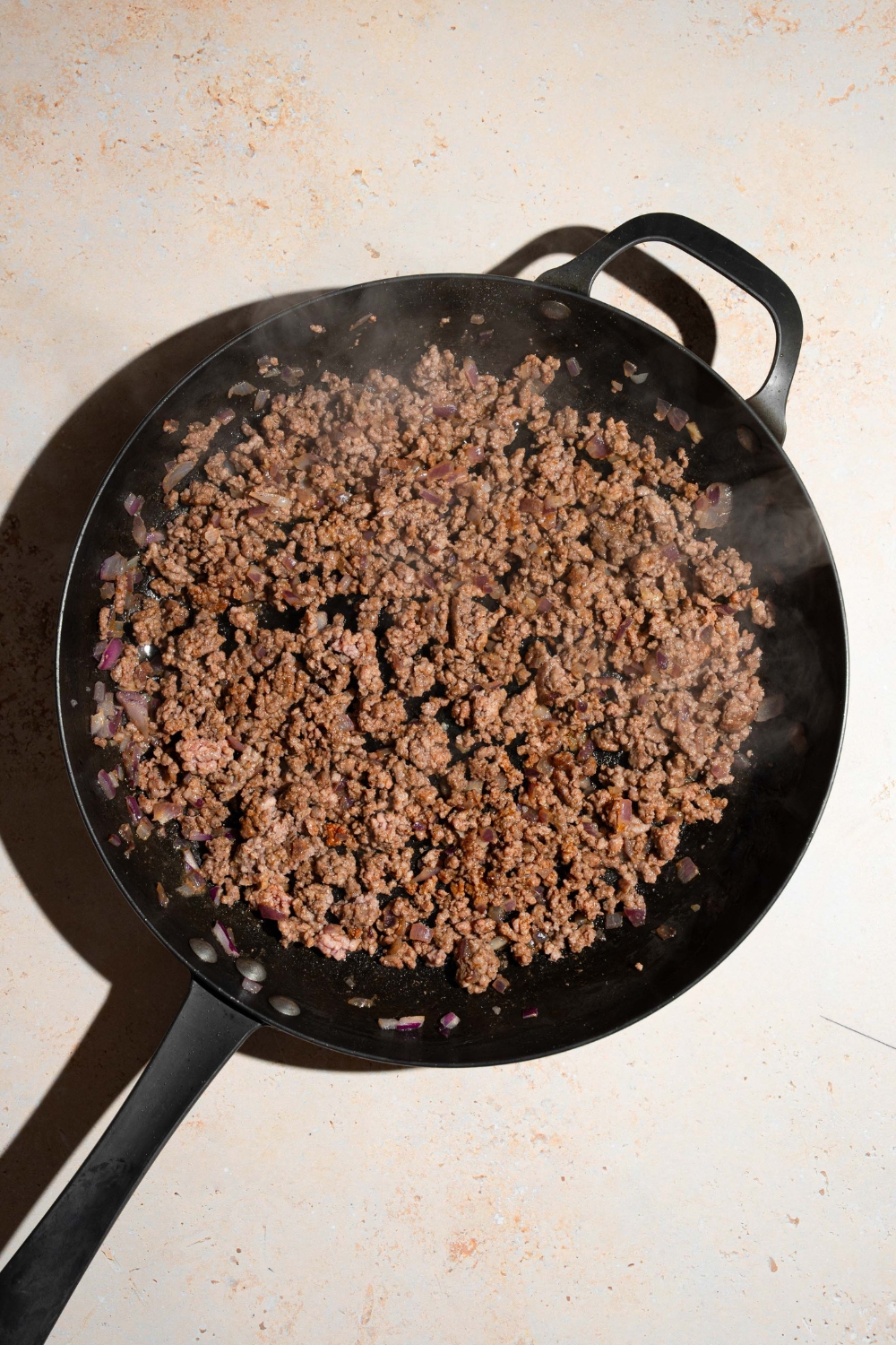 A skillet with cooked ground beef. The skillet is on a tan counter.