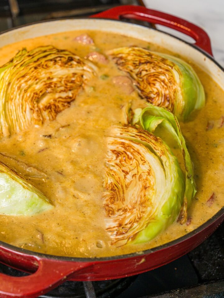 A skillet with smothered cabbage with sausage. The skillet is cooking on a stove.