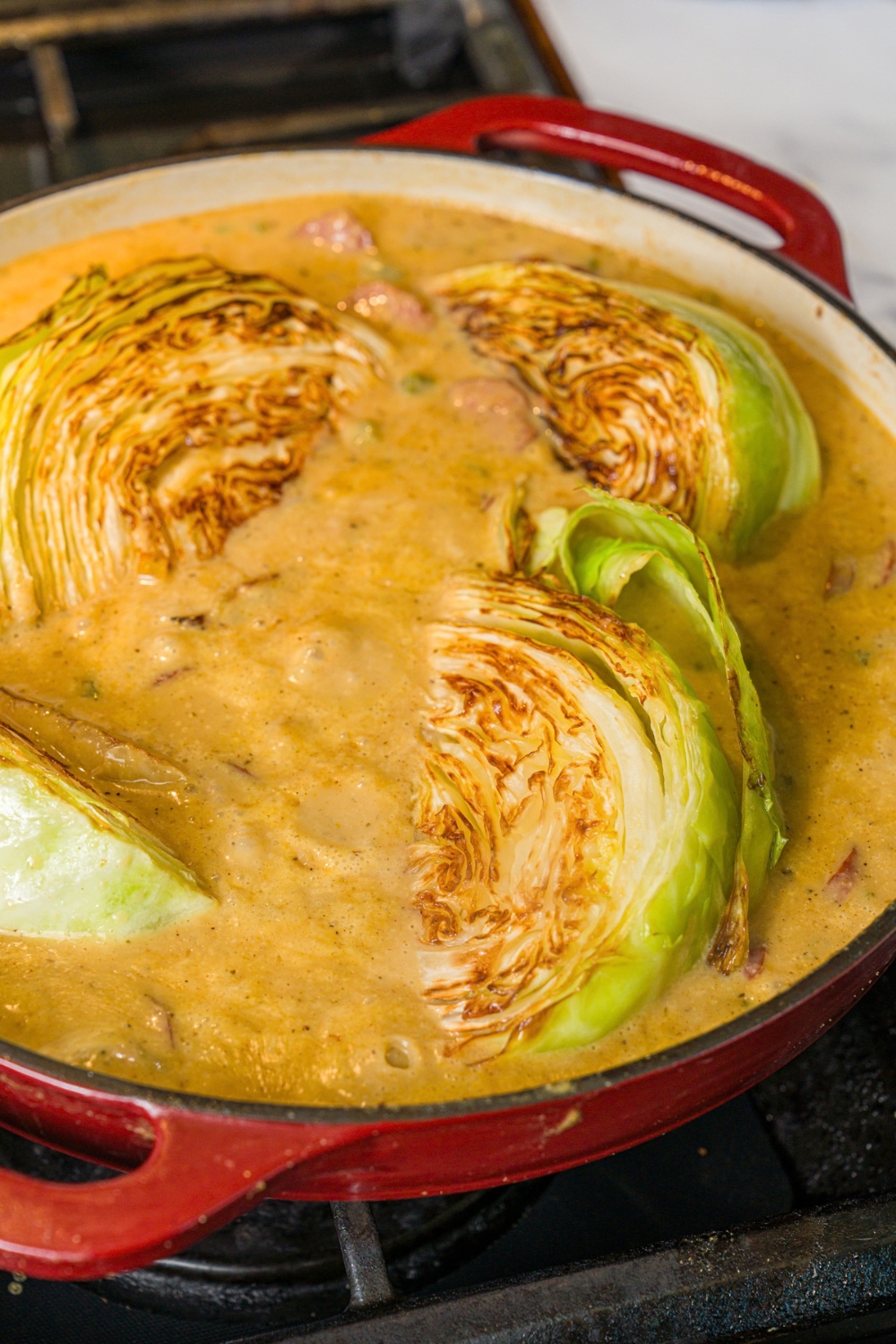 A skillet with smothered cabbage with sausage. The skillet is cooking on a stove.