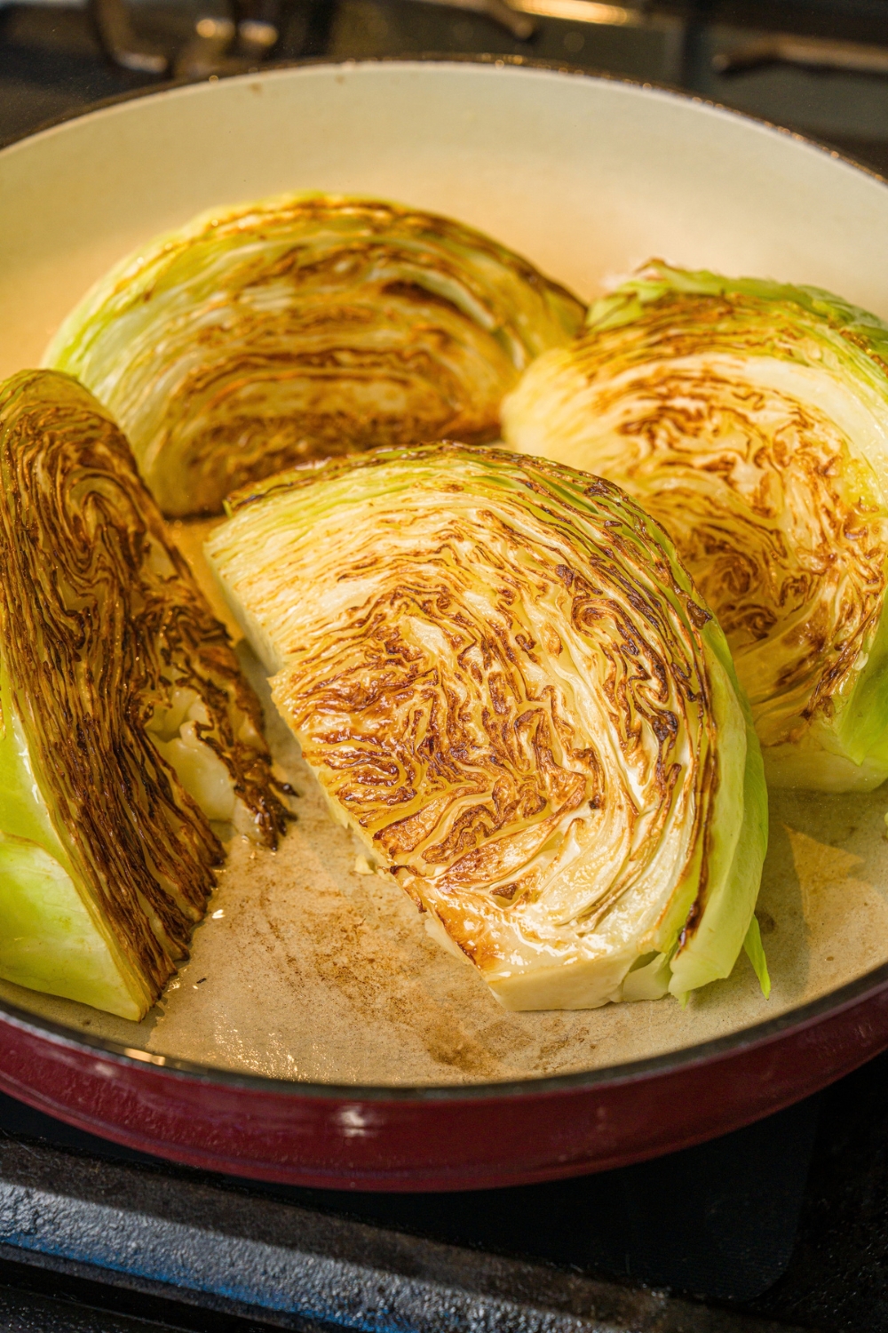 A skillet with quartered cabbage searing in oil. The skillet is cooking on a stove.