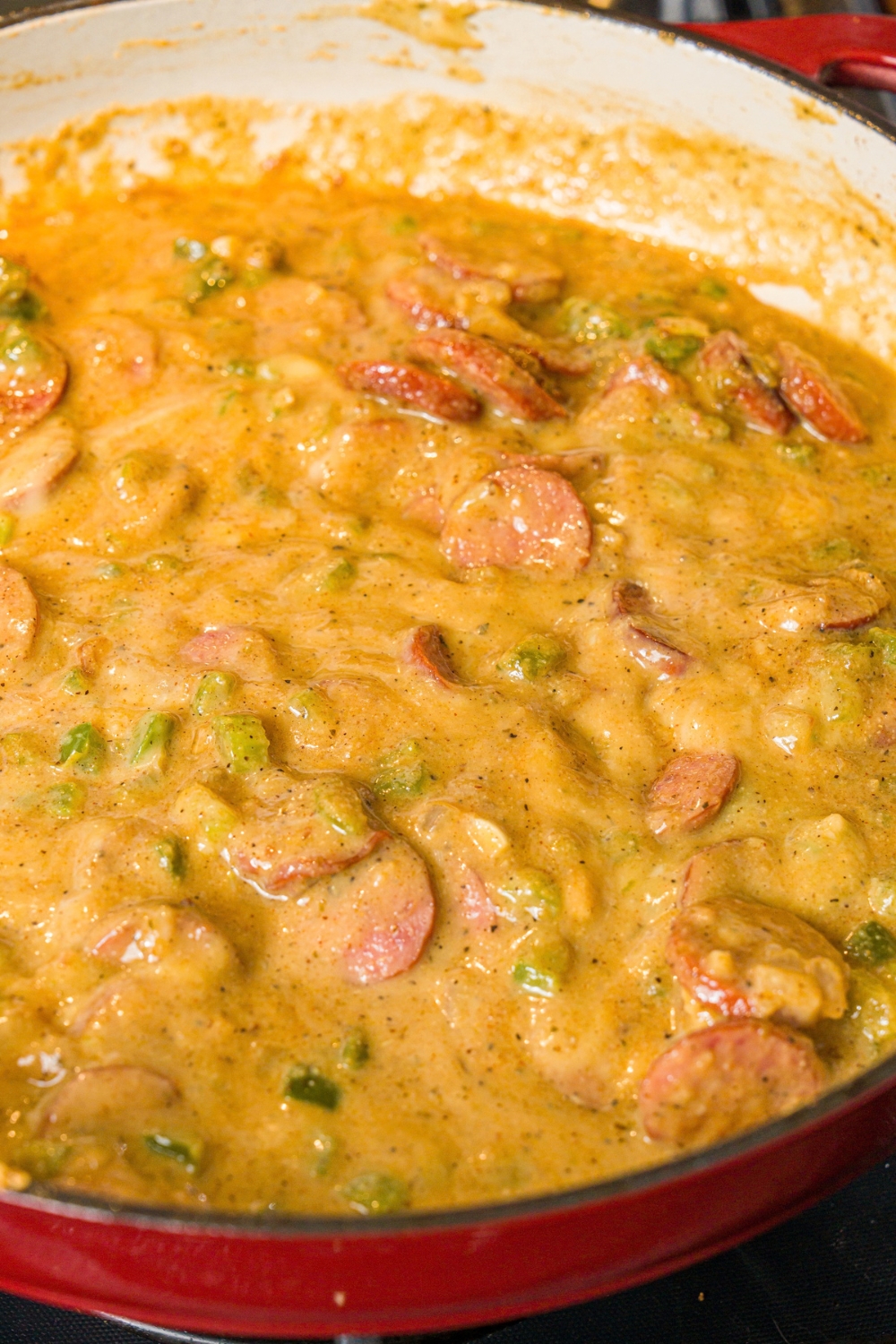 A skillet with smothered cabbage sauce with sausage. The skillet is cooking on a stove.