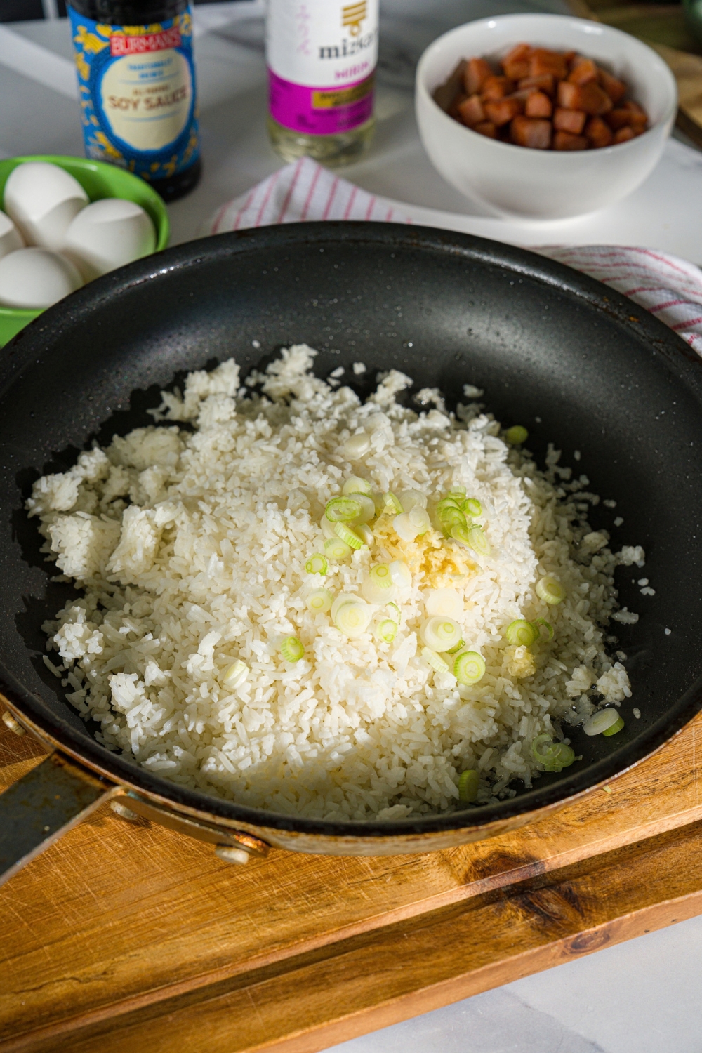 A skillet with toasted rice topped with garlic and onion whites. The skillet is on a wooden board.
