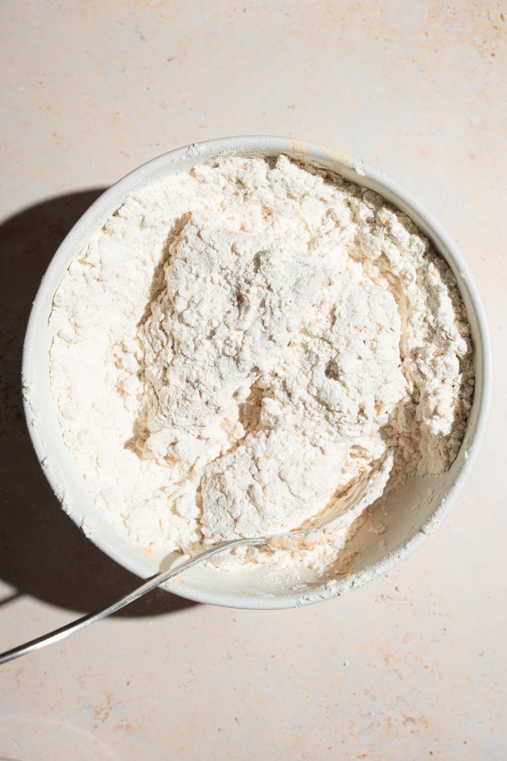 A large bowl of seasoned flour with marinated chicken tenders dredged in the bowl. The bowl is on a tan counter.