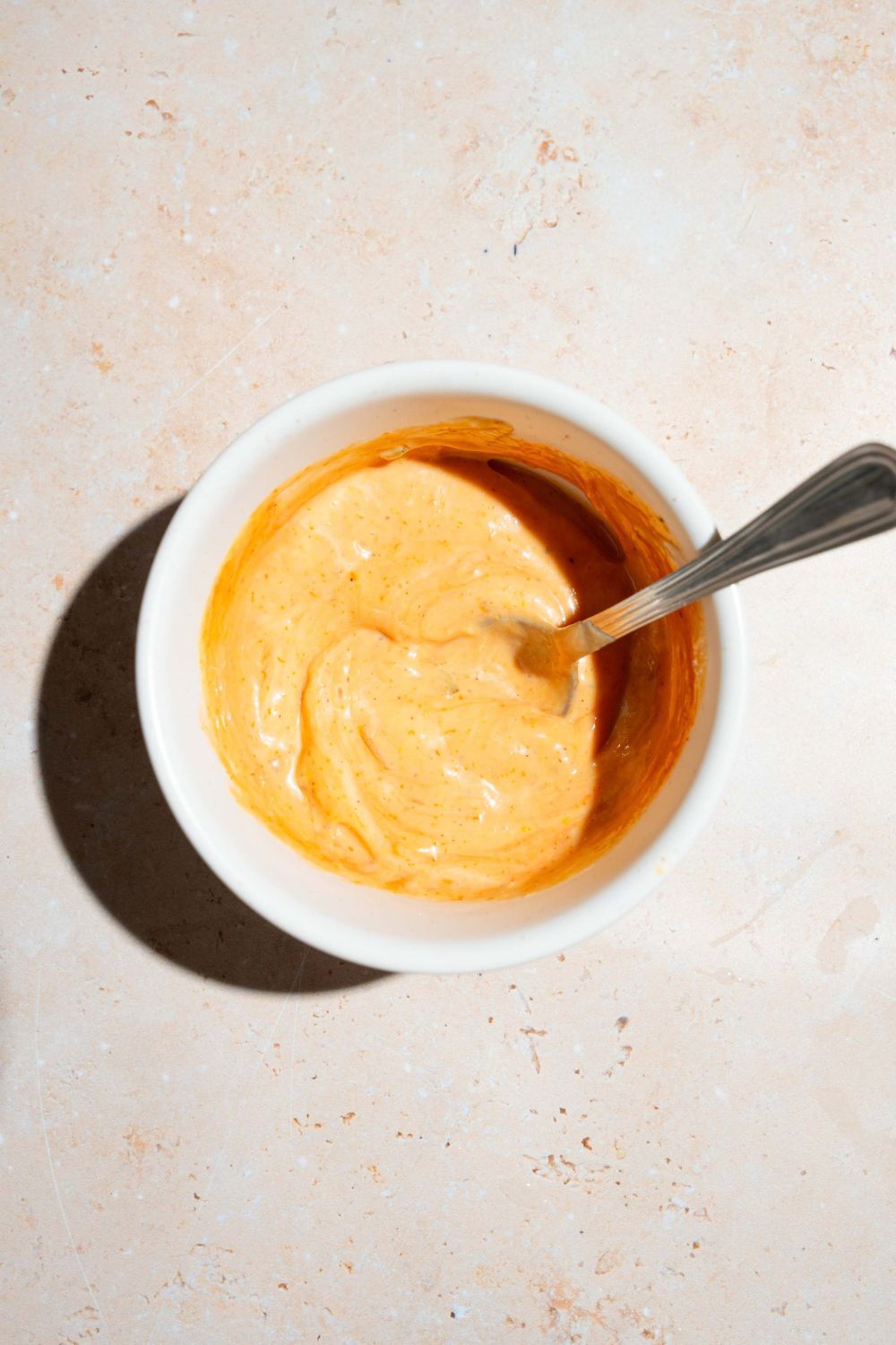 A small bowl of burger sauce with a spoon in the bowl. The bowl is on a tan counter.