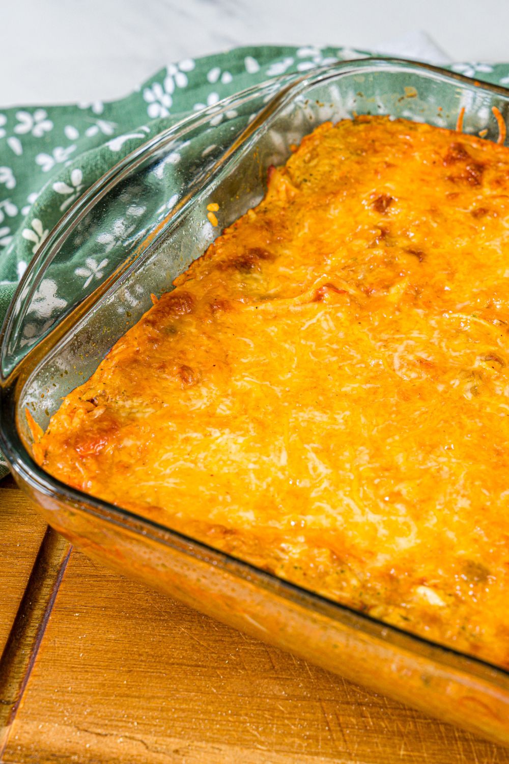 A baking dish with baked swim chicken and rice. The dish is on a wooden board with a green floral napkin.