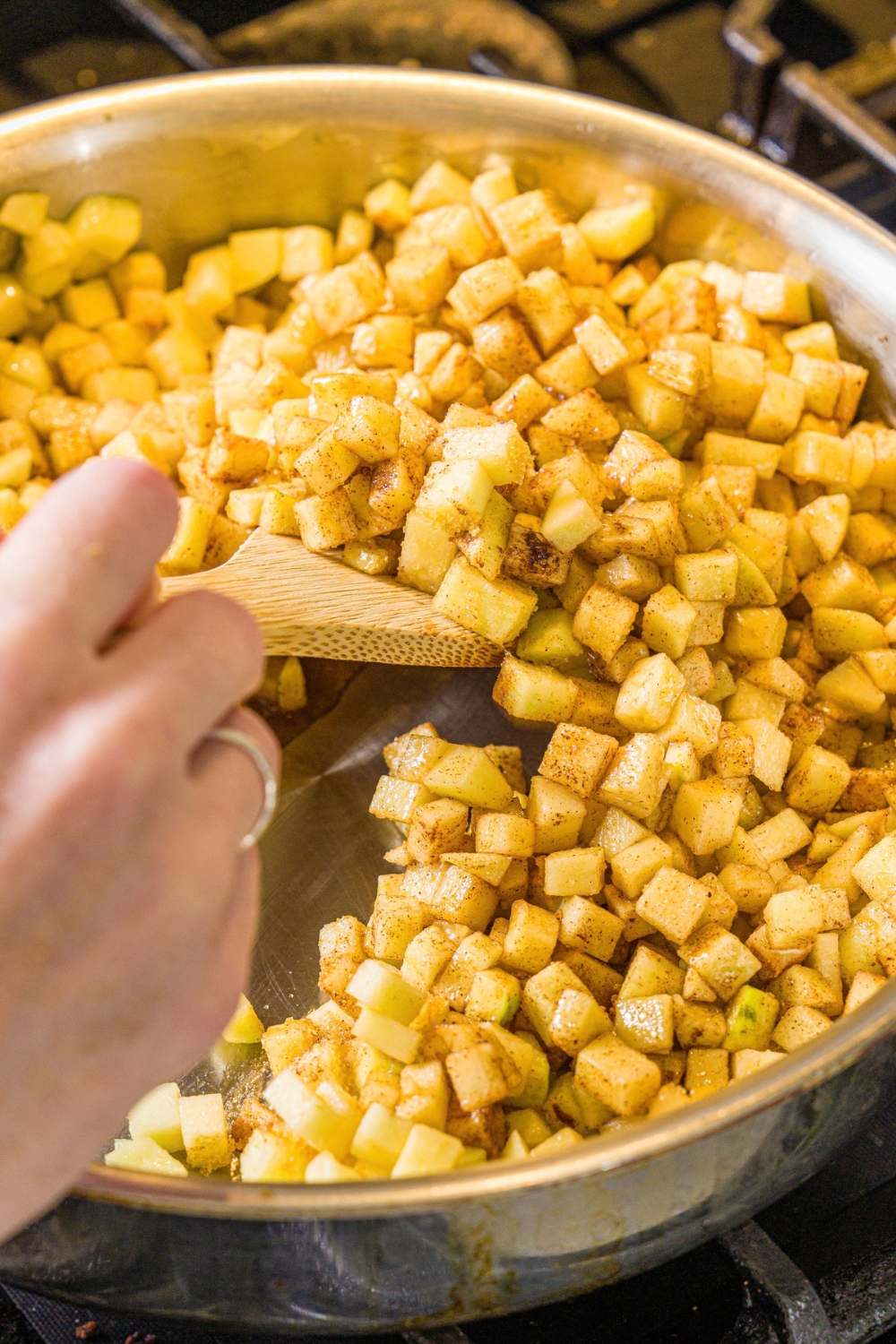 A skillet with a wooden spoon mixing an apple pie filling mixture. The skillet is cooking on the stove.