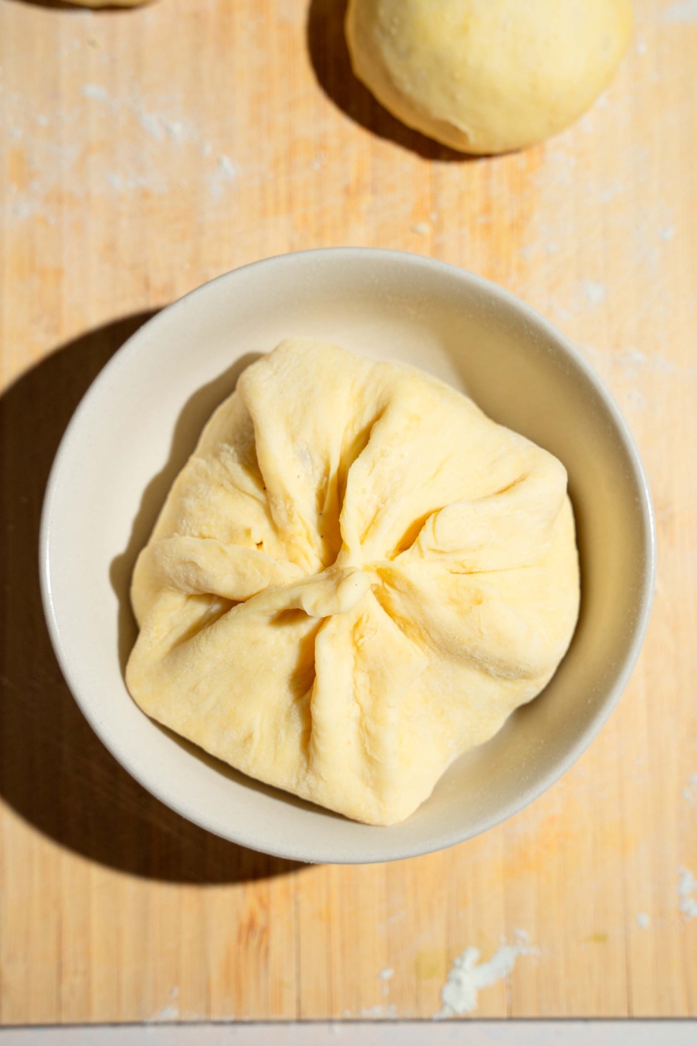 A small dough ball shaped in a ramekin with the edges closed around a burger filling. The bowl is on a wooden board.