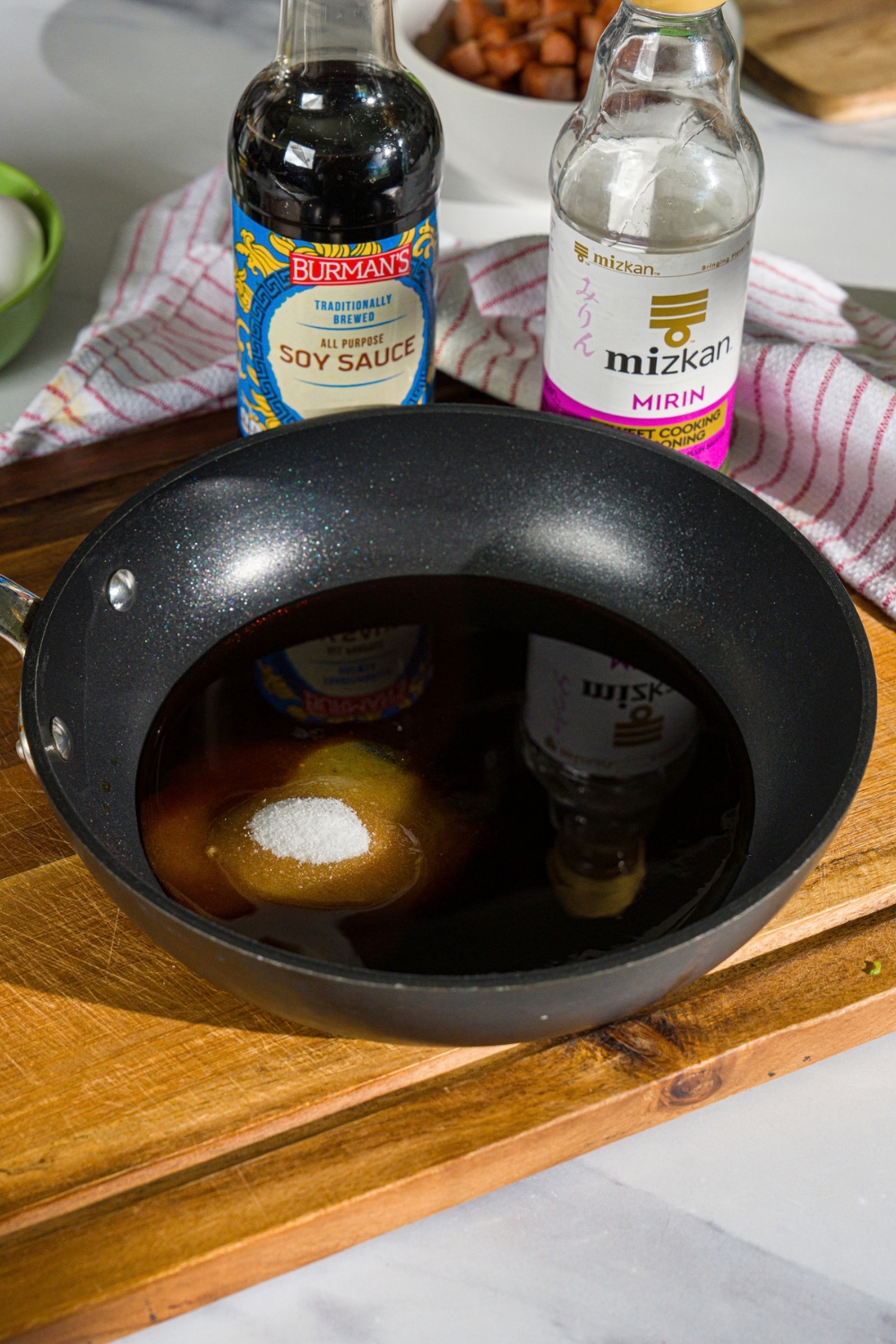 A skillet with spam musubi sauce including soy sauce, mirin, and sugar. The skillet is on a wooden board.