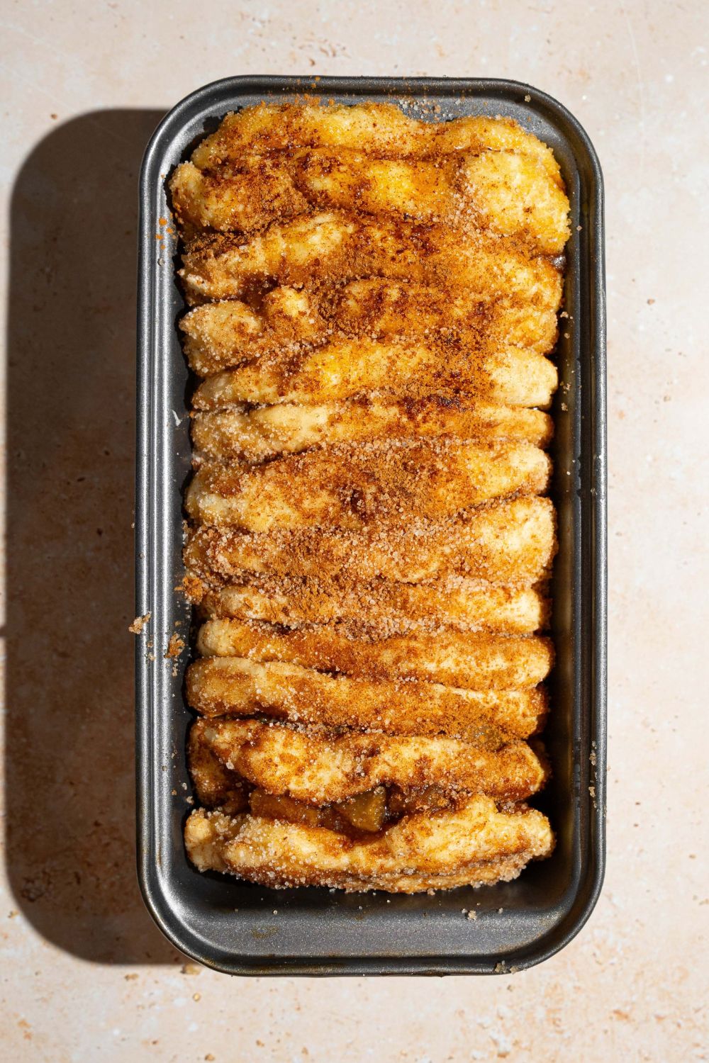 Several apple pie biscuits coated in cinnamon sugar lined up in a loaf pan. The pan is on a tan counter.