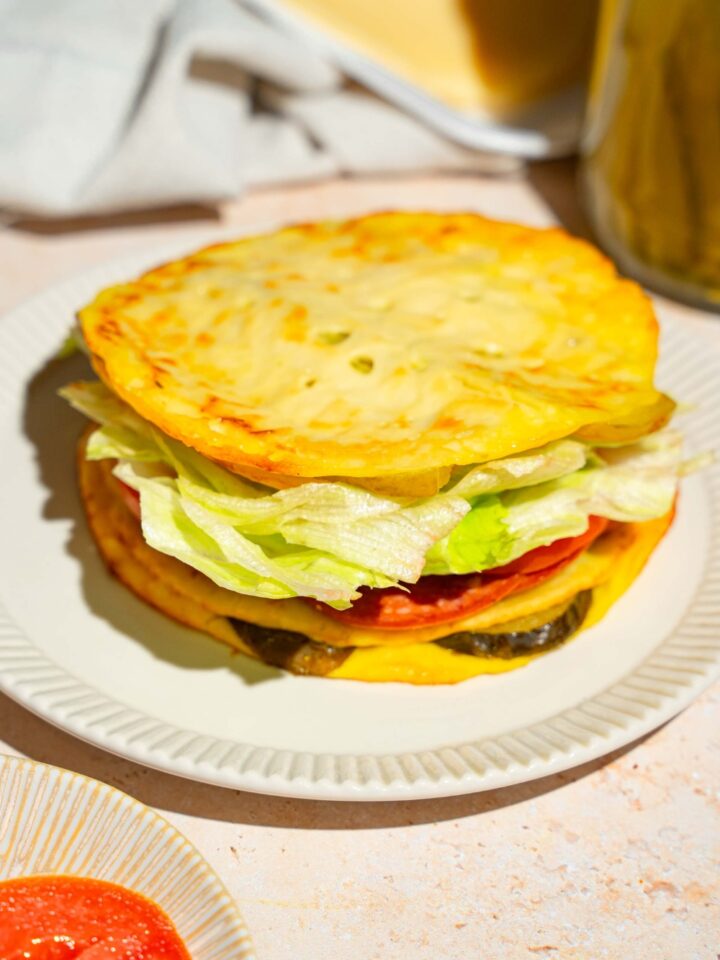 A white plate with a sandwich made with pickle bread, lettuce, tomato, and deli meat. The plate is on a tan counter.